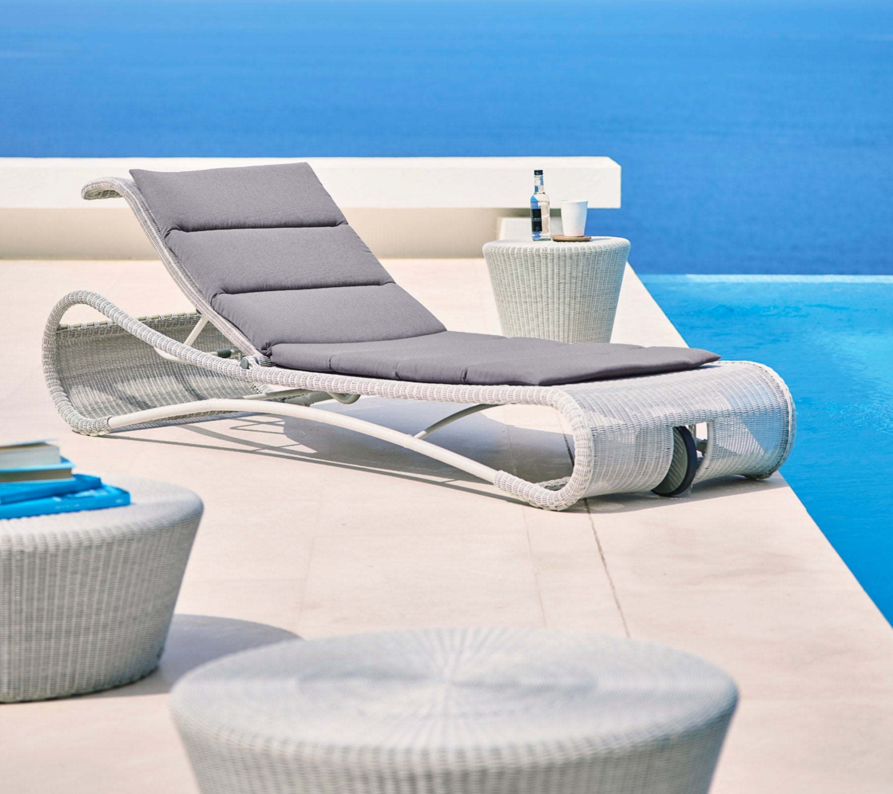Chaise longue élégante avec coussin gris à côté de tables d'appoint modernes, sur fond bleu serein. Parfaite pour se détendre.