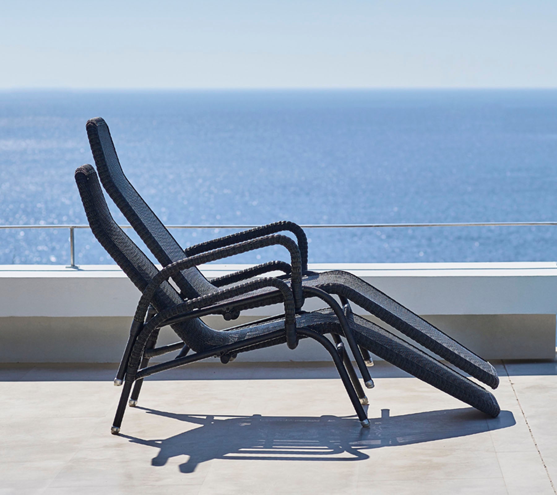Trois chaises longues sont empilées contre un arrière-plan de vue sereine sur l'océan, montrant un espace de relaxation en plein air minimaliste.