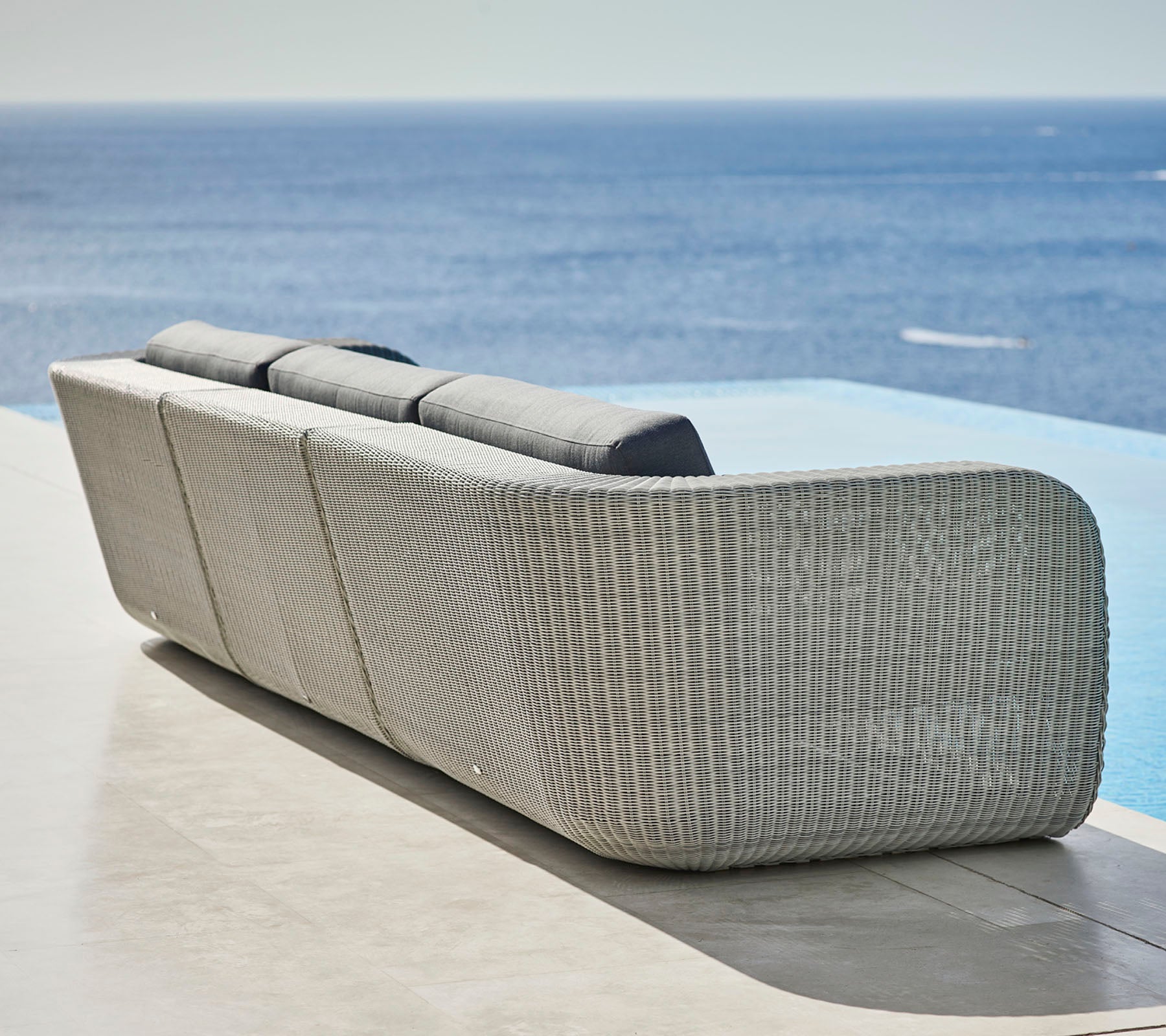 Canapé tissé élégant avec un design courbé et des coussins moelleux, surplombant une vue paisible sur l'océan. Idéal pour la détente et les espaces extérieurs.