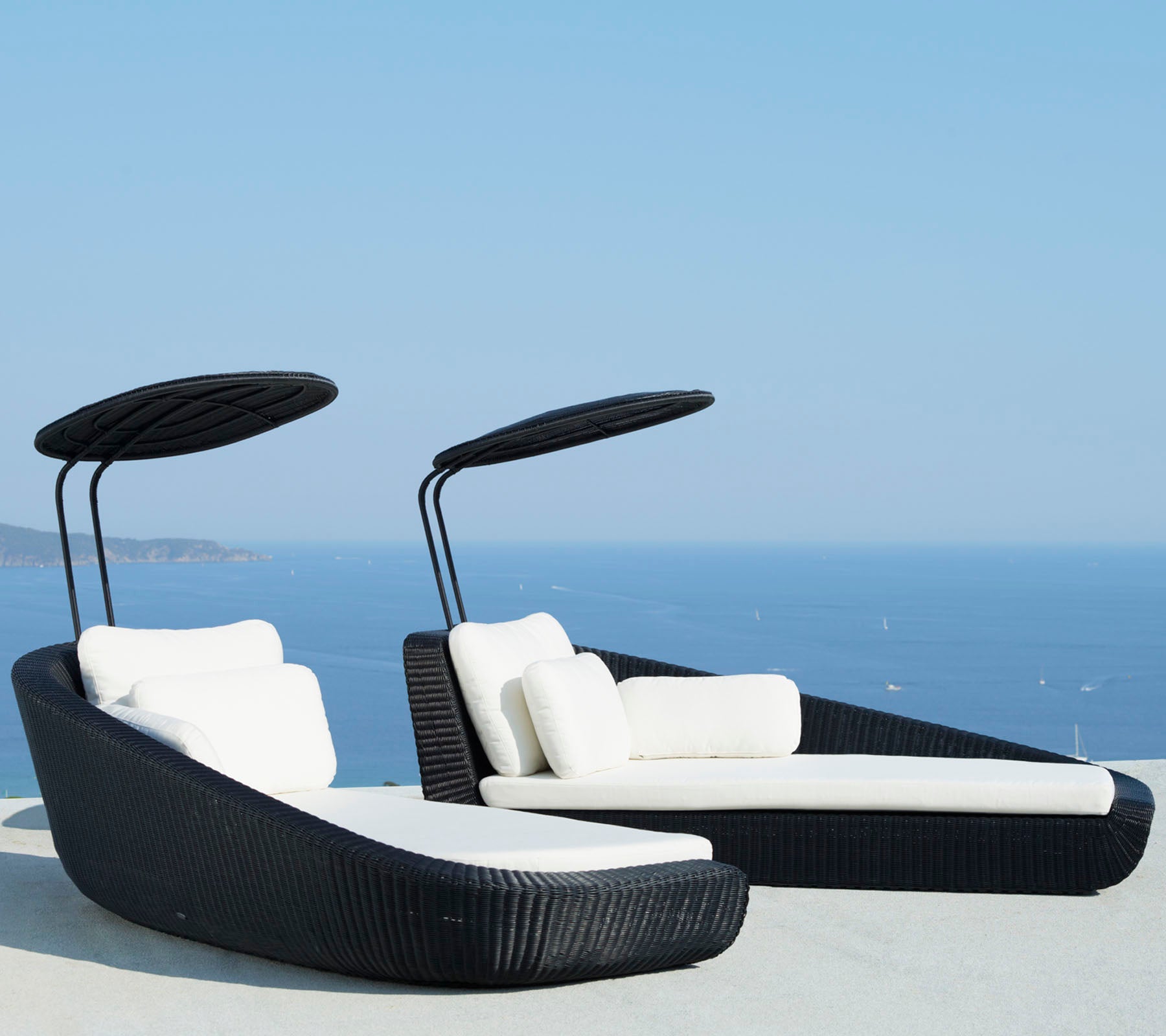 Deux chaises longues élégantes avec des coussins blancs et des auvents courbés, sur fond d'un océan bleu pittoresque.