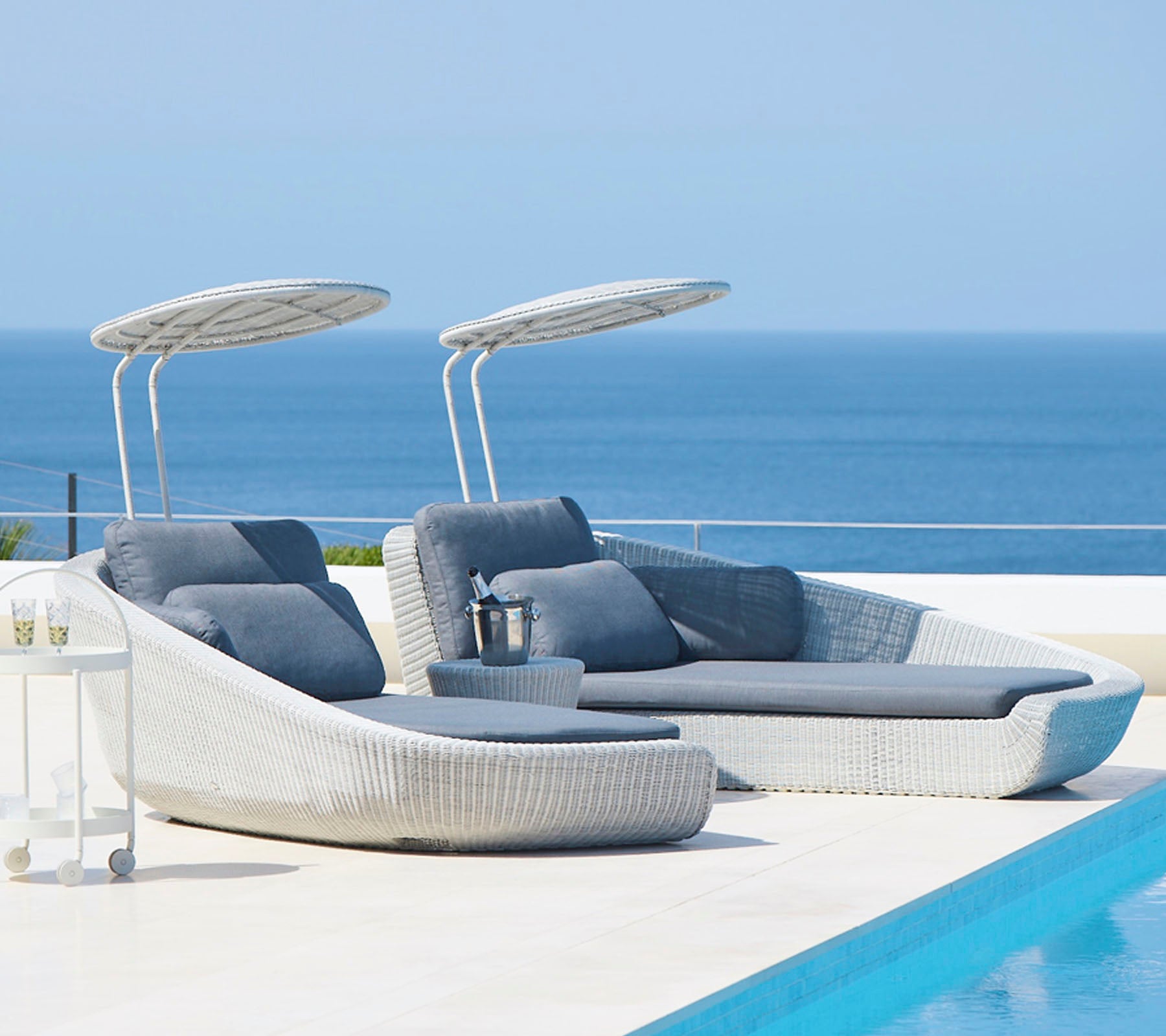 Chaises longues élégantes en extérieur avec auvents à côté d'une piscine sereine, surplombant une mer tranquille. Parfait pour la détente et les loisirs.