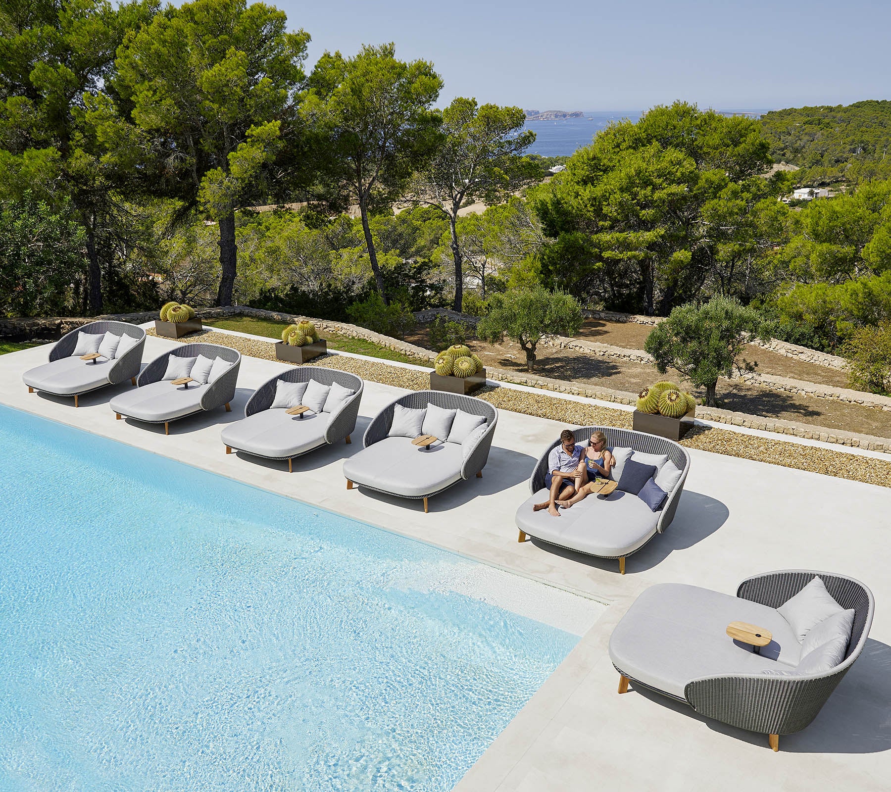 Des chaises longues sont disposées autour d'une piscine avec une vue pittoresque sur la verdure et les arbres en arrière-plan. Une personne se détend sur l'une des chaises.