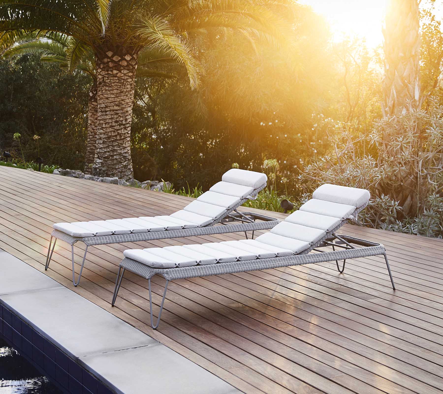 Deux chaises longues élégantes avec des coussins blancs, positionnées à côté d'une piscine et entourées d'une végétation luxuriante, profitant de la chaleur du soleil.