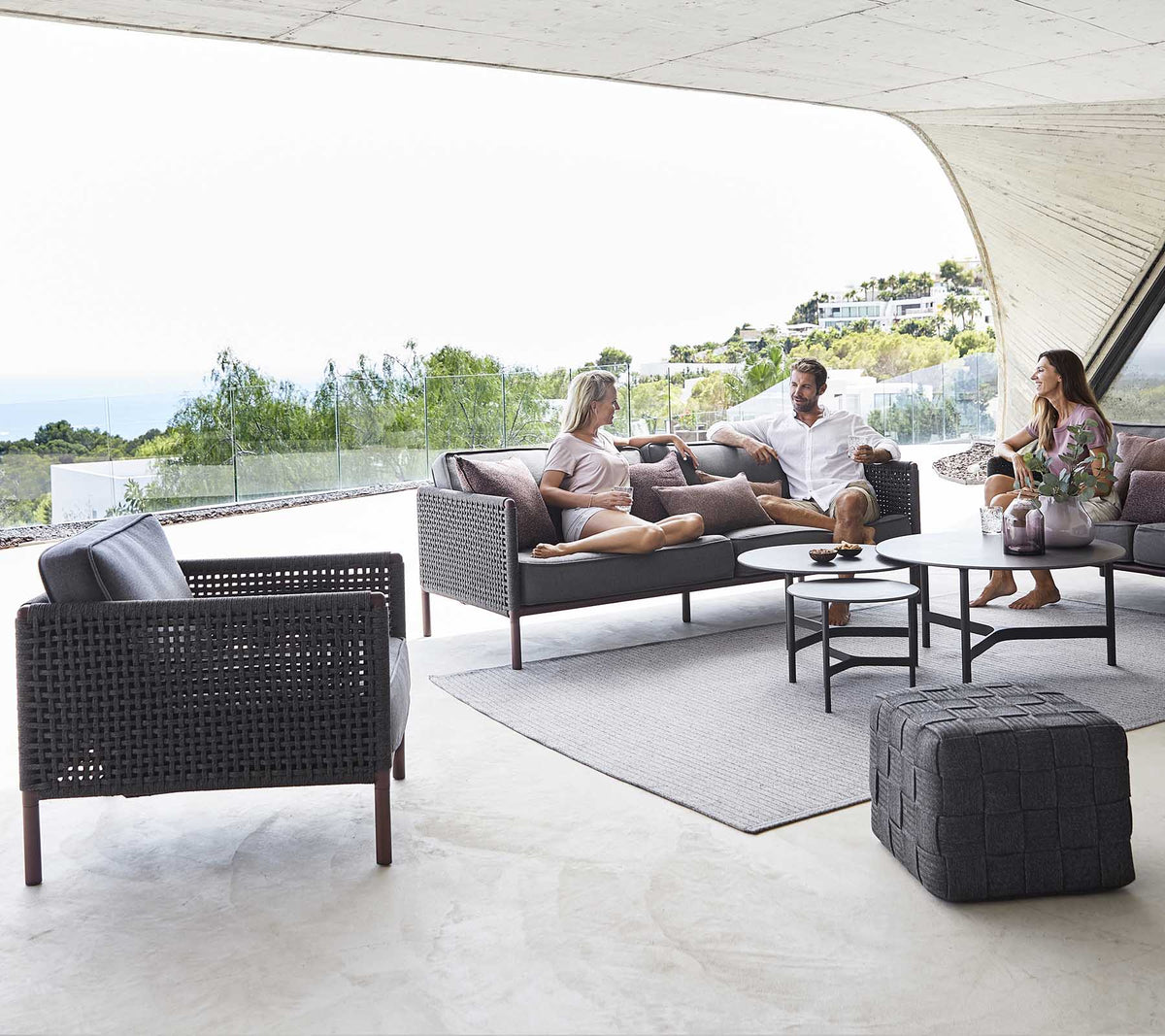 Un coin salon confortable avec une table basse, des chaises élégantes et des personnes profitant d'une conversation détendue sur fond de paysage pittoresque.