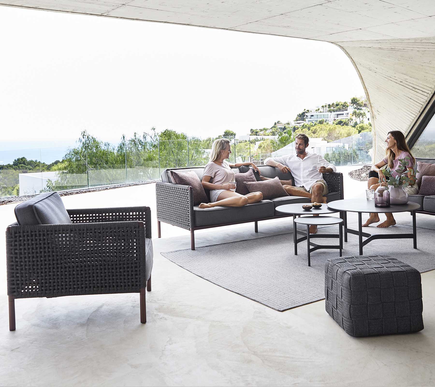 Un coin salon confortable avec une table basse, des chaises élégantes et des personnes profitant d'une conversation détendue sur fond de paysage pittoresque.
