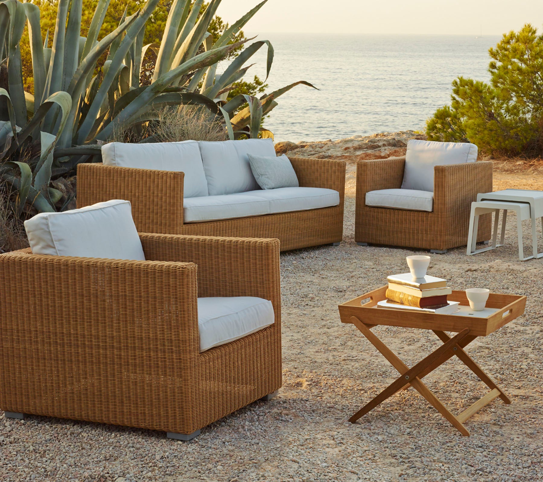 Agencement extérieur élégant avec des chaises en rotin tressé et un canapé avec des coussins légers, complété par une table basse en bois.