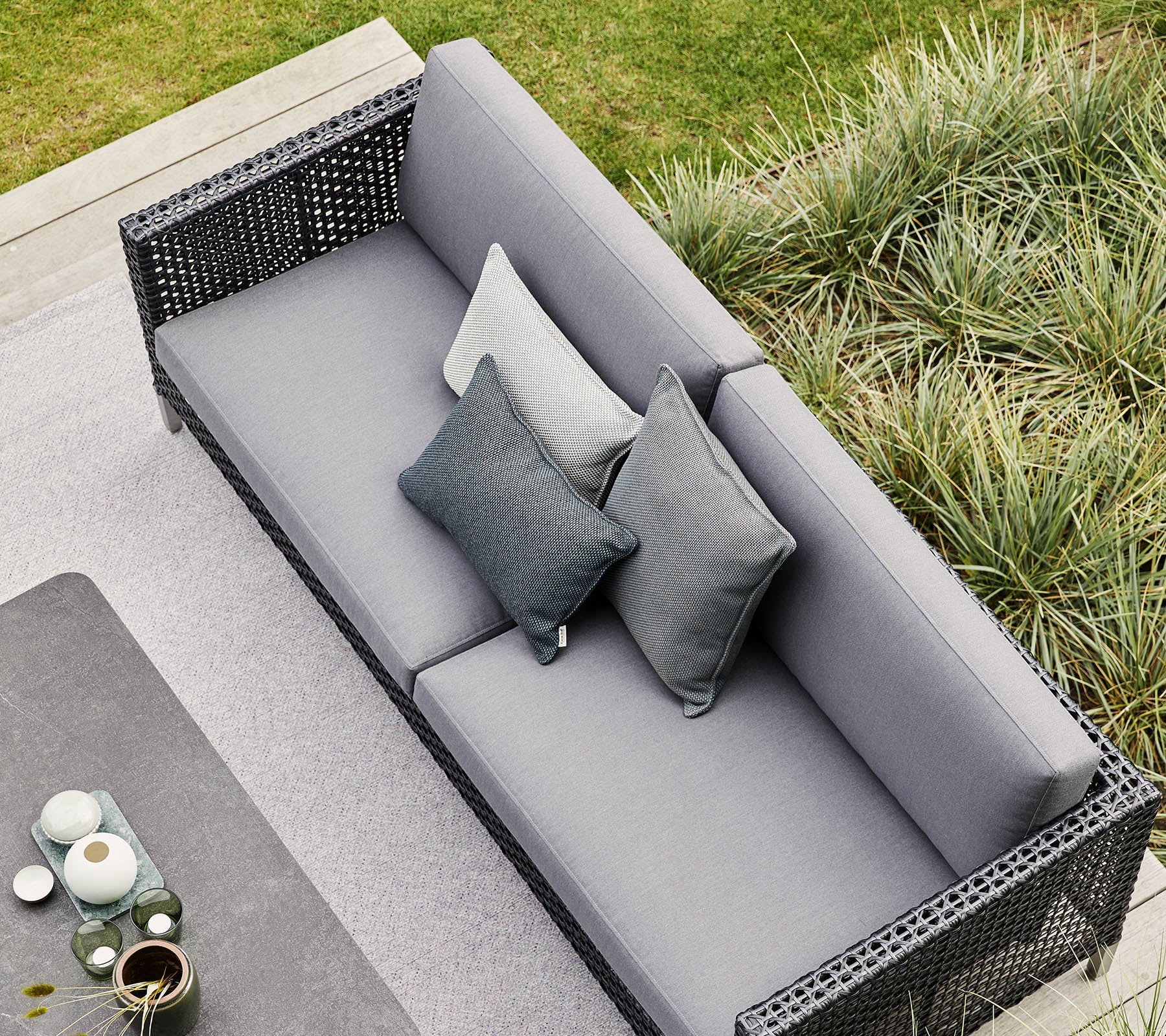 Canapé gris élégant avec des coussins décoratifs, entouré de verdure luxuriante et d'éléments décoratifs modernes. Parfait pour se détendre et se réunir.
