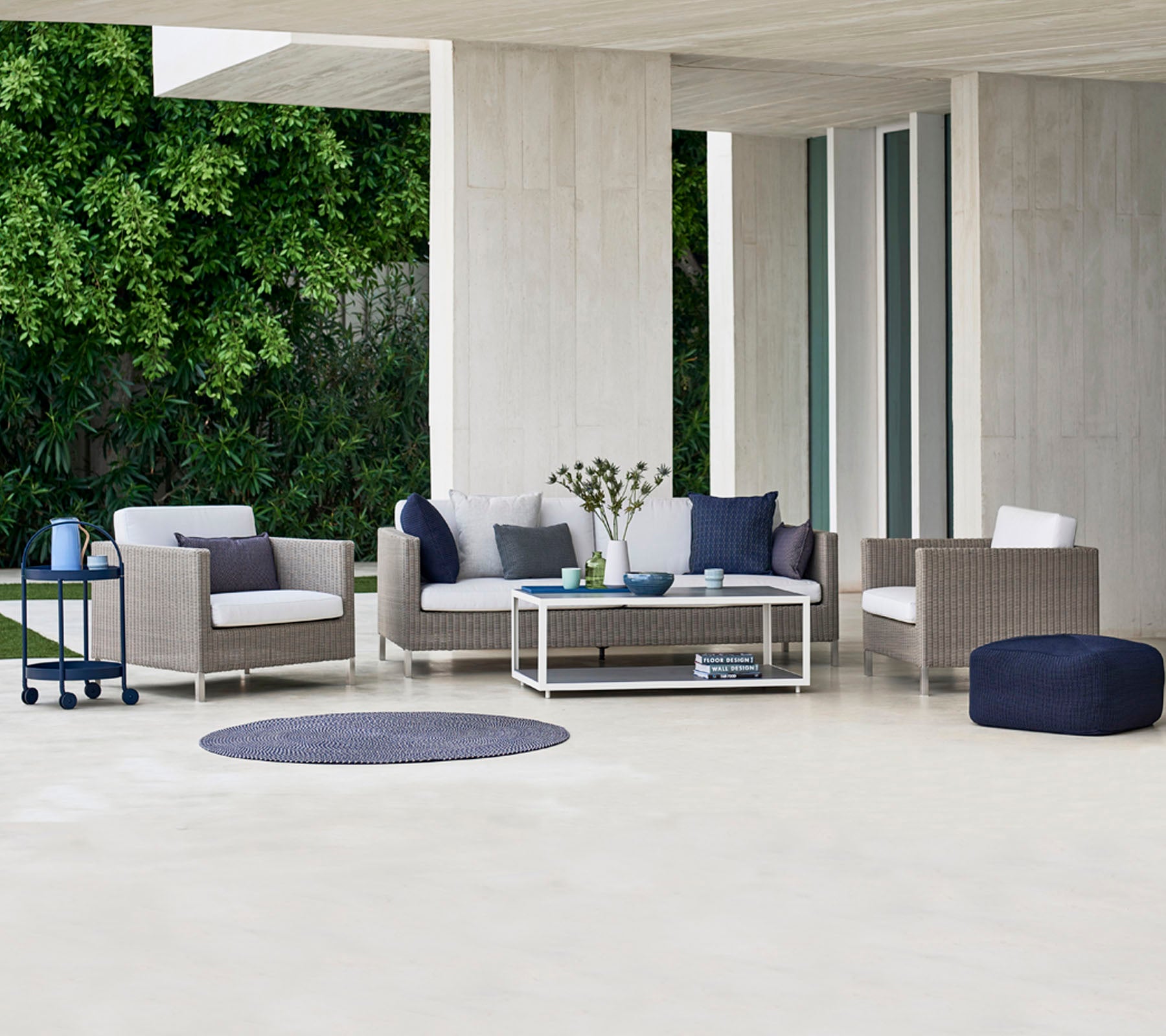 Espace extérieur contemporain avec un canapé, des fauteuils et une table basse, agrémenté de coussins décoratifs et d'un tapis rond.