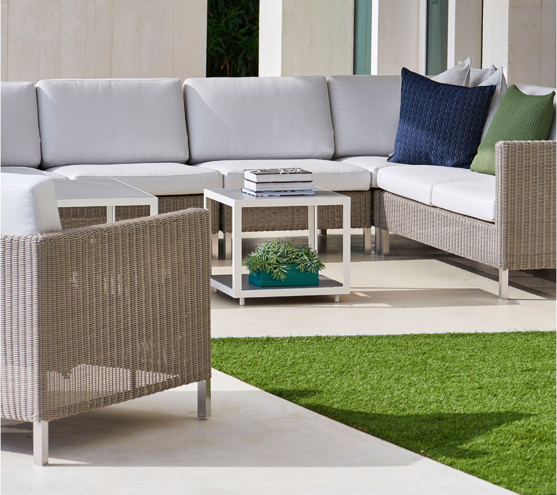Espace extérieur élégant avec un canapé d'angle avec des coussins gris, des coussins confortables et une table basse moderne sur une surface verte luxuriante.