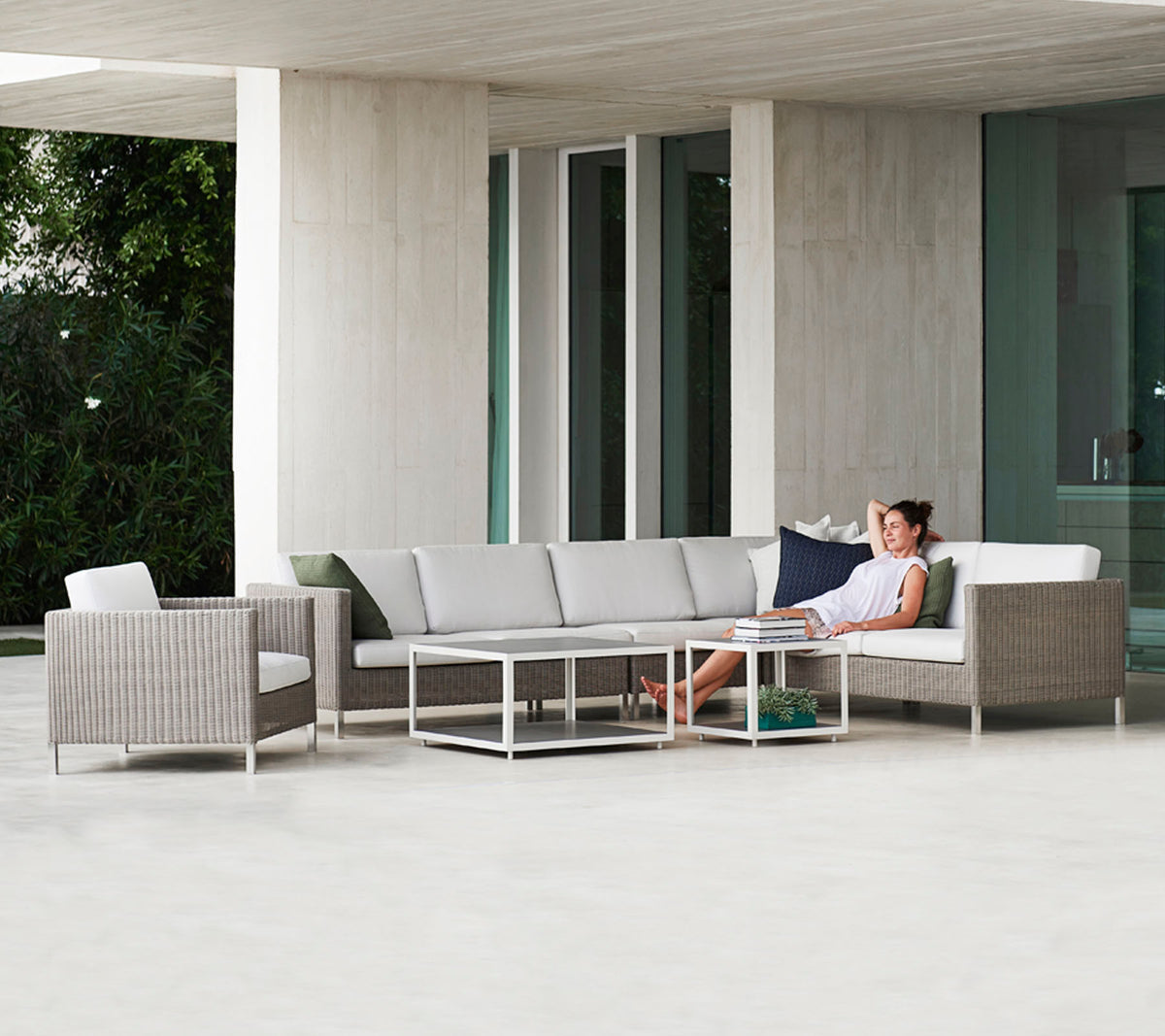 Un aménagement moderne avec un canapé sectionnel gris, une table en verre et une chaise en osier, où une personne se détend confortablement.