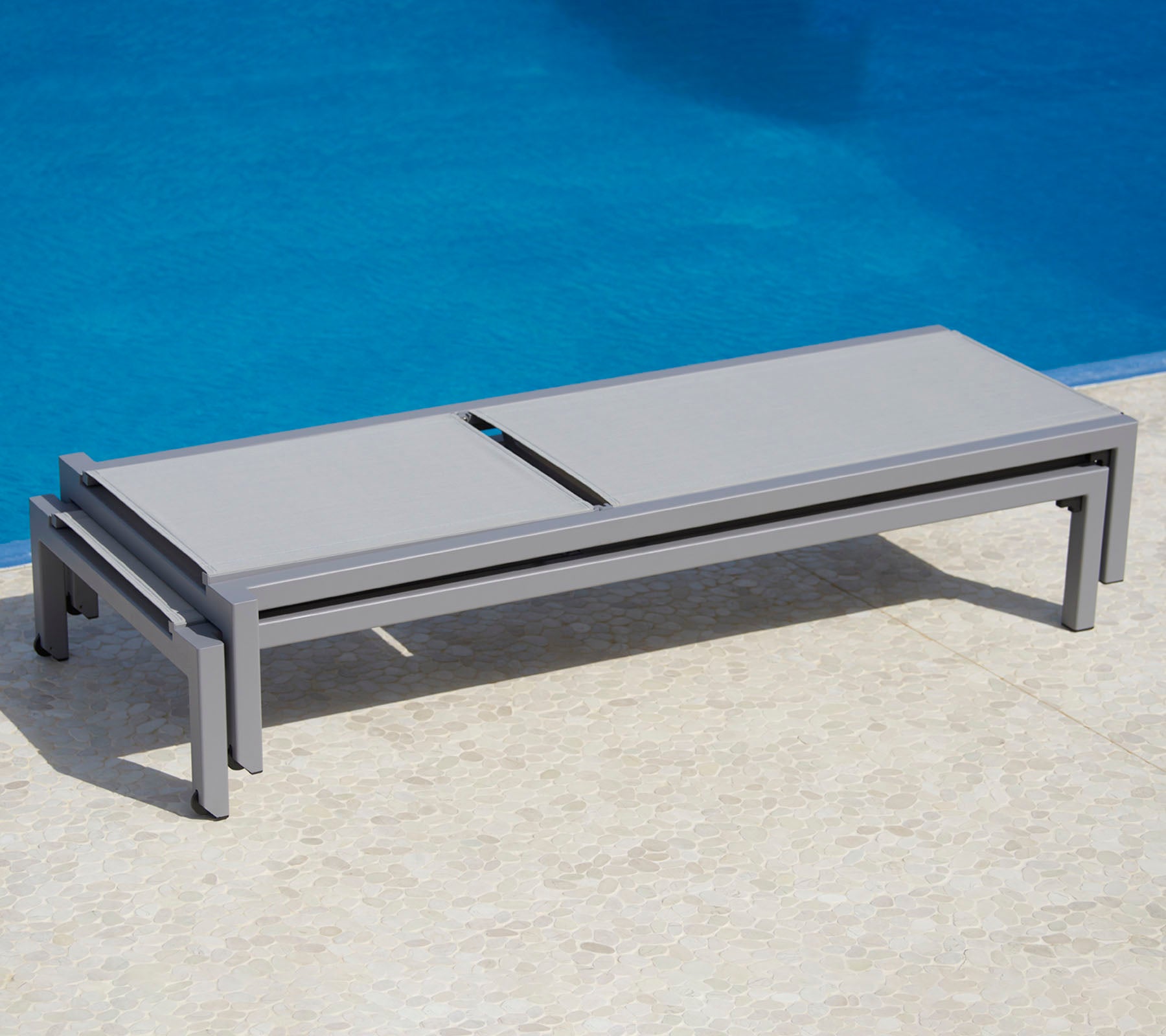 Lit de salon gris élégant à côté d'une piscine, offrant un design épuré et une fonctionnalité pratique pour la détente.