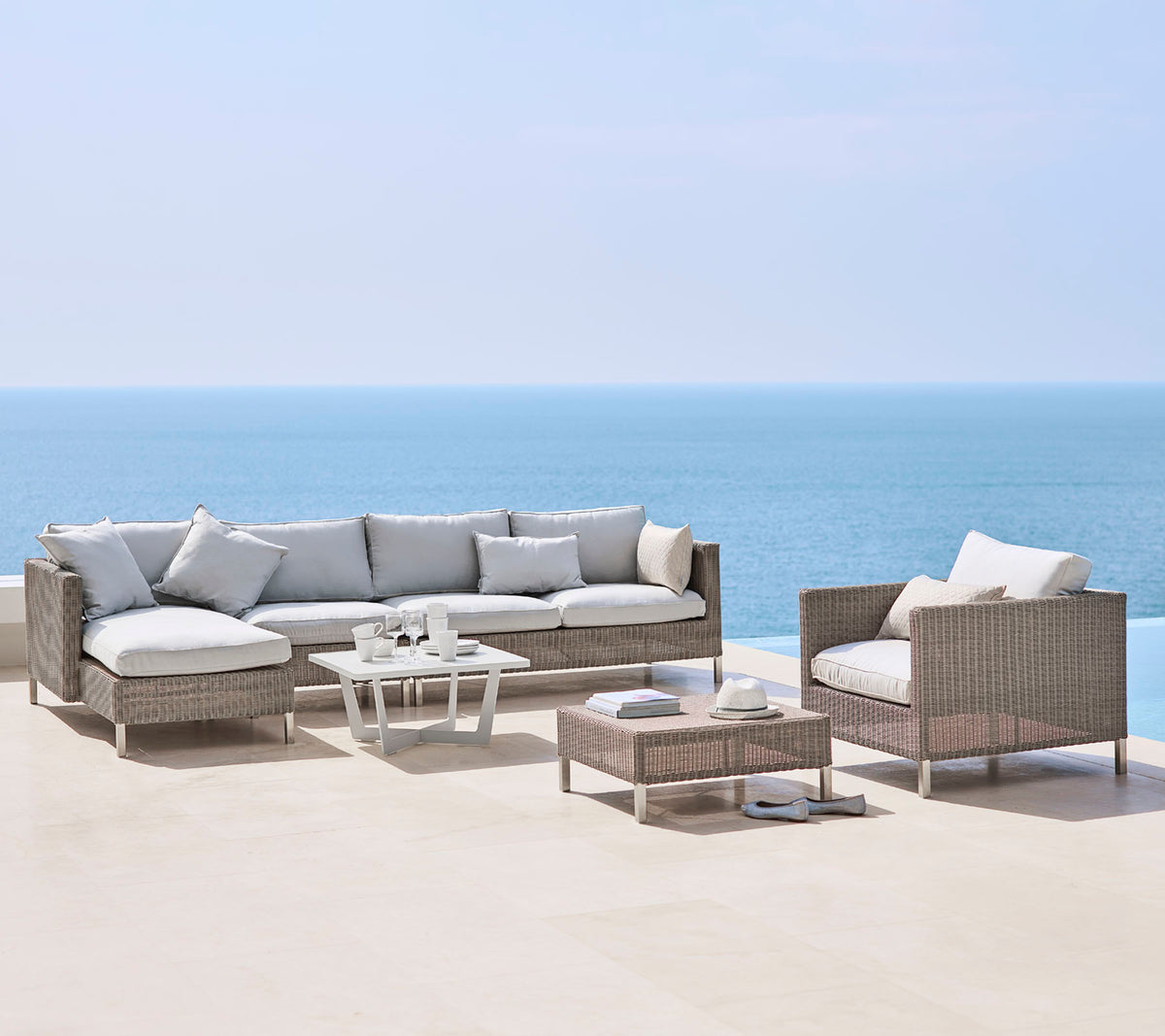 Un aménagement de sièges extérieur élégant avec un grand canapé, un fauteuil et une table basse, tous dotés de coussins clairs et de matériaux tissés, au bord de la mer.