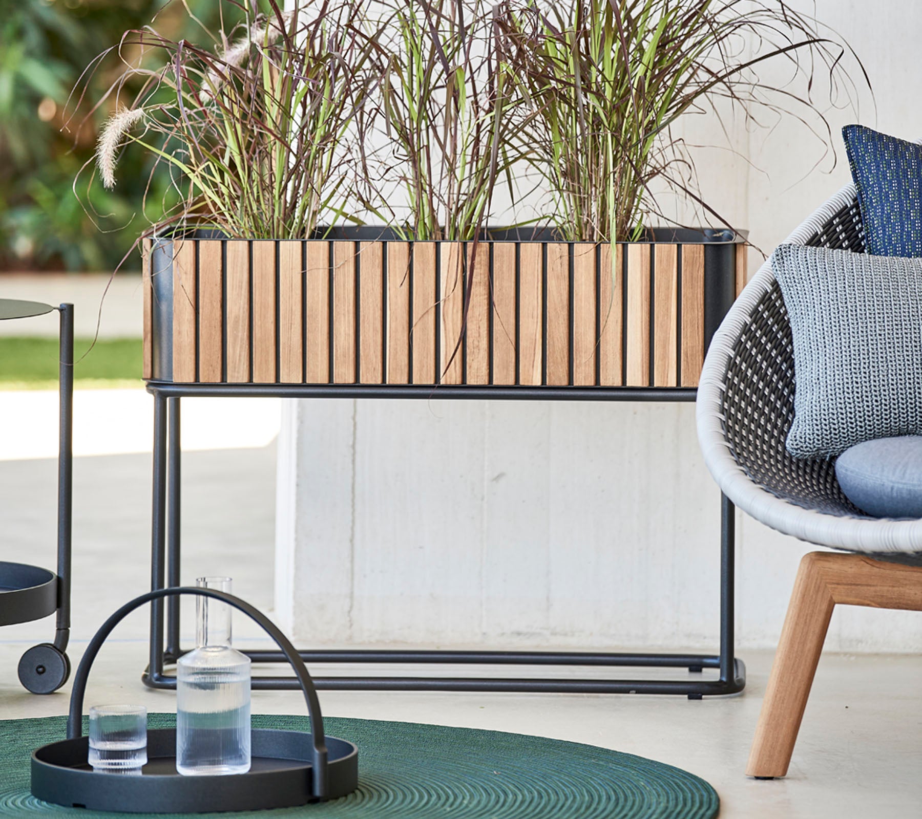 Boîte à fleurs en bois avec des plantes décoratives, accompagnée d'un plateau rond contenant des verres et d'une chaise moderne avec des coussins moelleux.