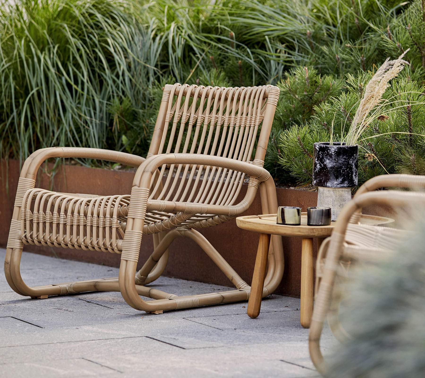 Une chaise tissée naturellement accompagnée d'une petite table en bois et d'éléments décoratifs, entourée de verdure luxuriante.