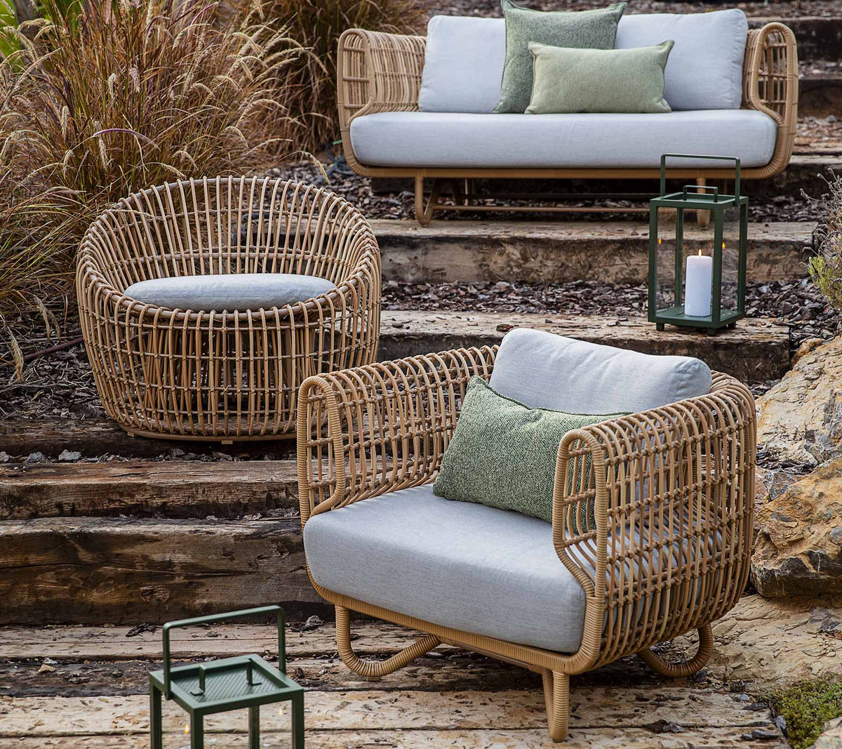 Une collection de meubles en osier tressé comprenant un canapé, une chaise et un siège rond, rehaussée de coussins et de lanternes.