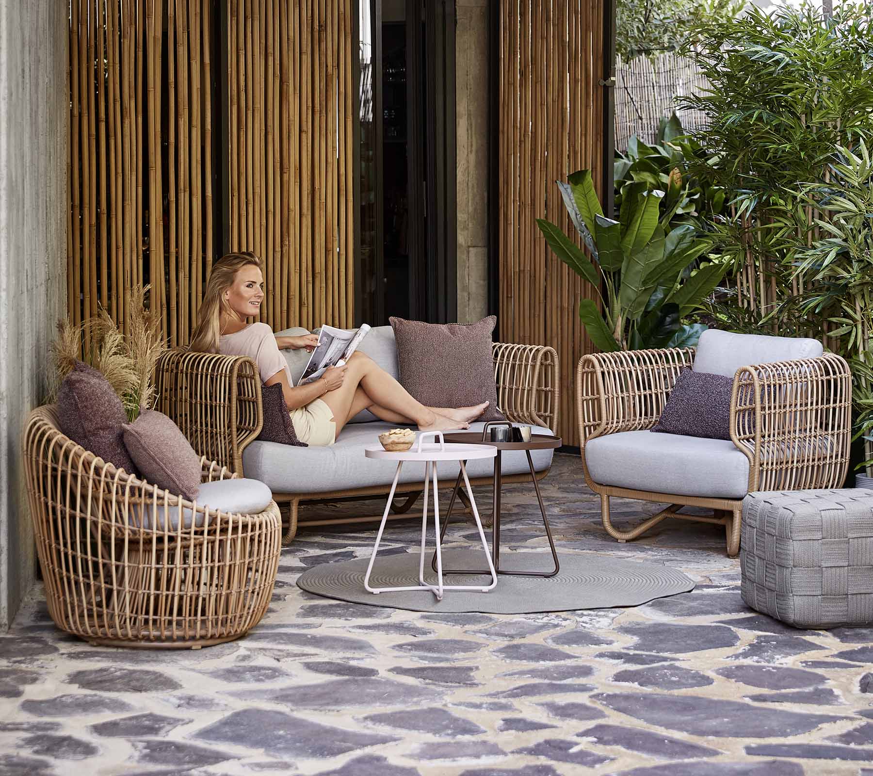 Un agencement de sièges élégant avec des meubles tissés, des coussins et une table basse, situé parmi la verdure et des éléments décoratifs.