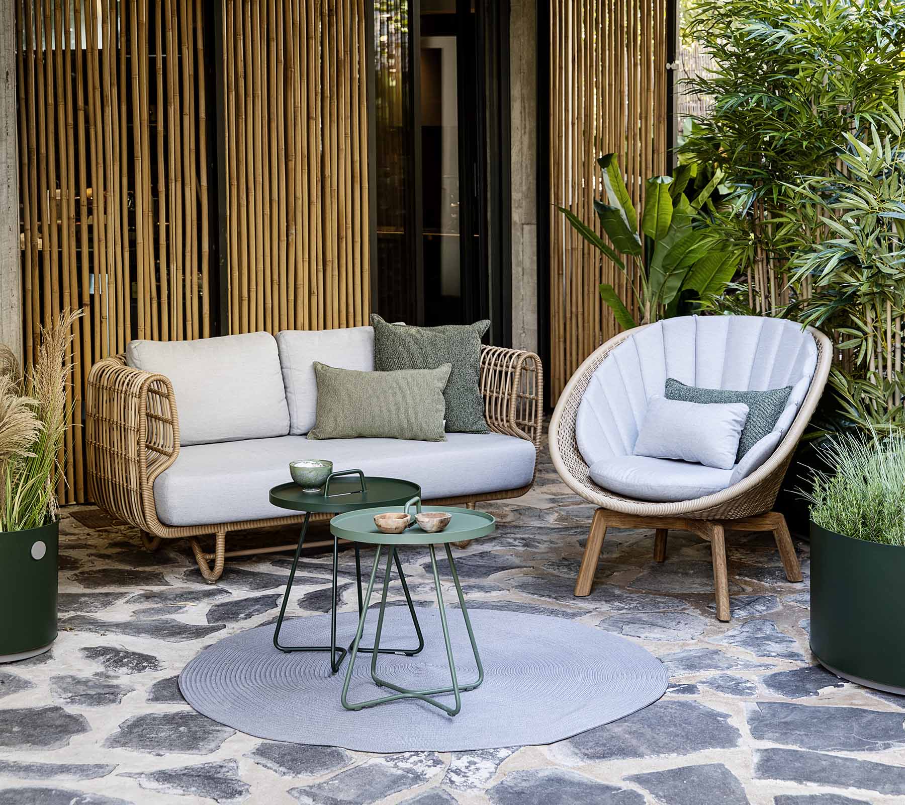 Un agencement de sièges confortable avec un canapé en rotin et une chaise élégante, accompagné d'une petite table et de plantes décoratives.