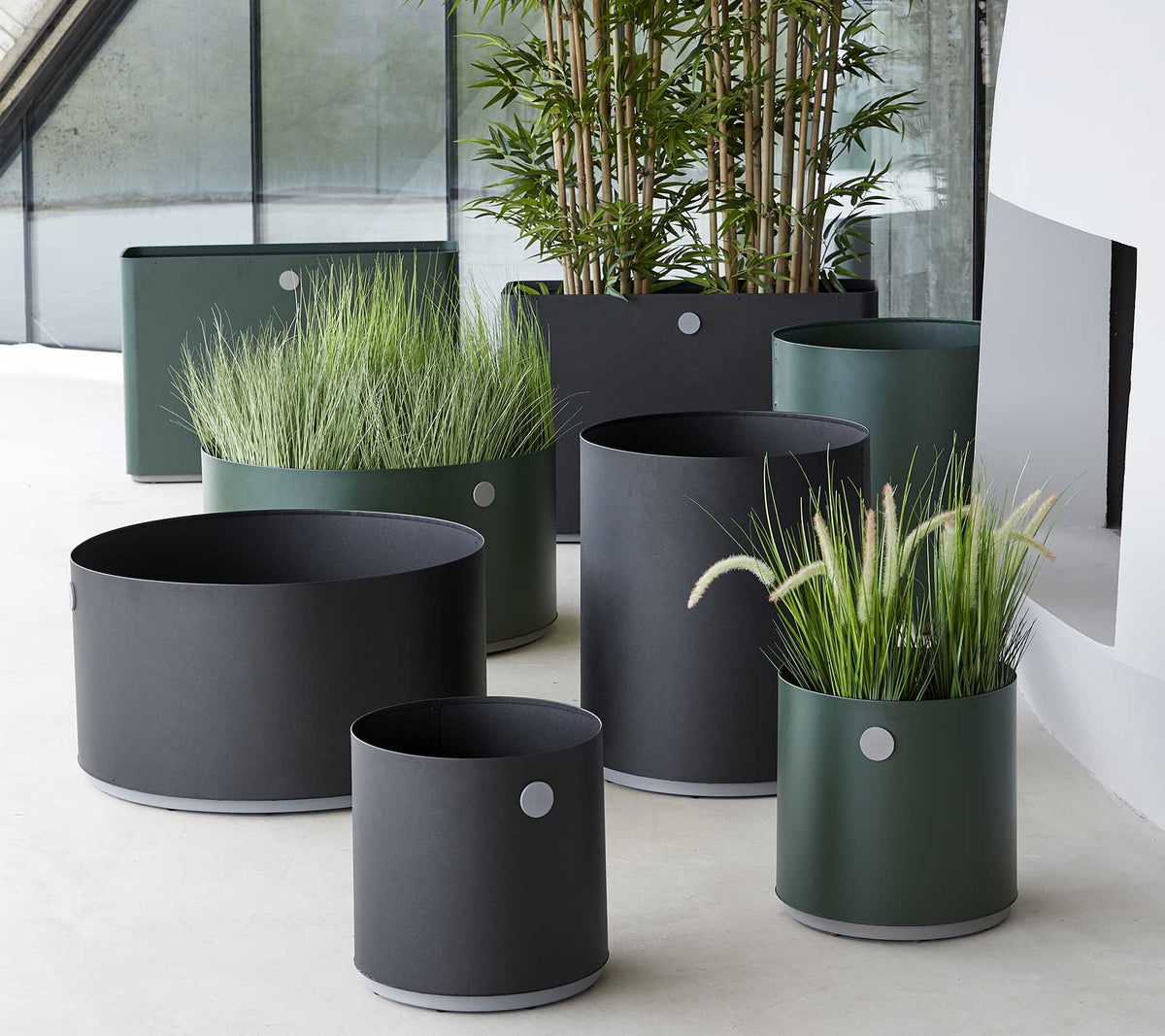 Diverses jardinières modernes en tons sombres, mettant en vedette des graminées ornementales et des plantes, disposées dans un cadre élégant.