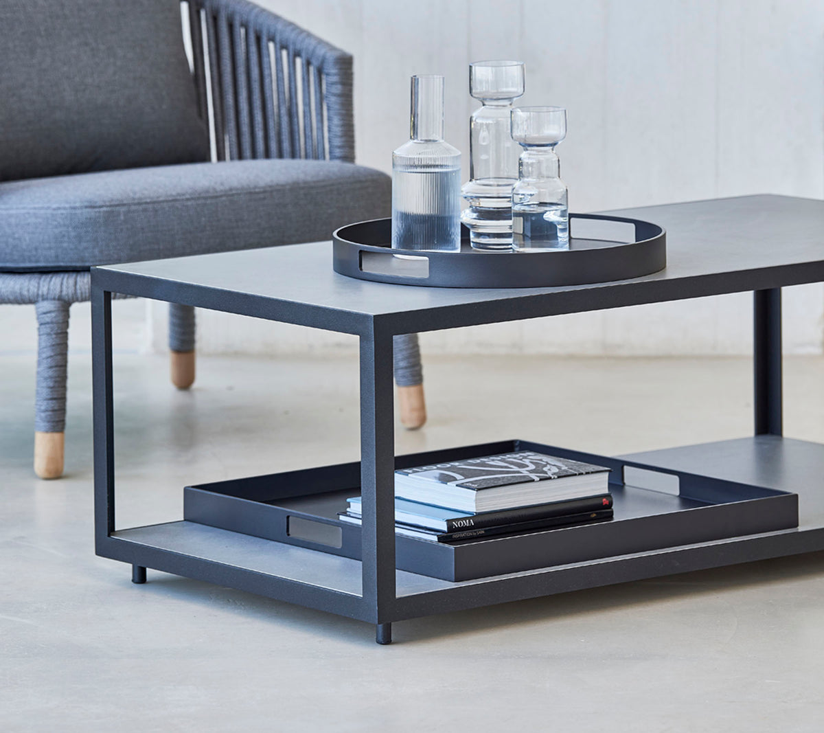 Table basse moderne au design épuré, avec un plateau, des verres et des livres sur l'étagère inférieure. Idéal pour des espaces de vie élégants.