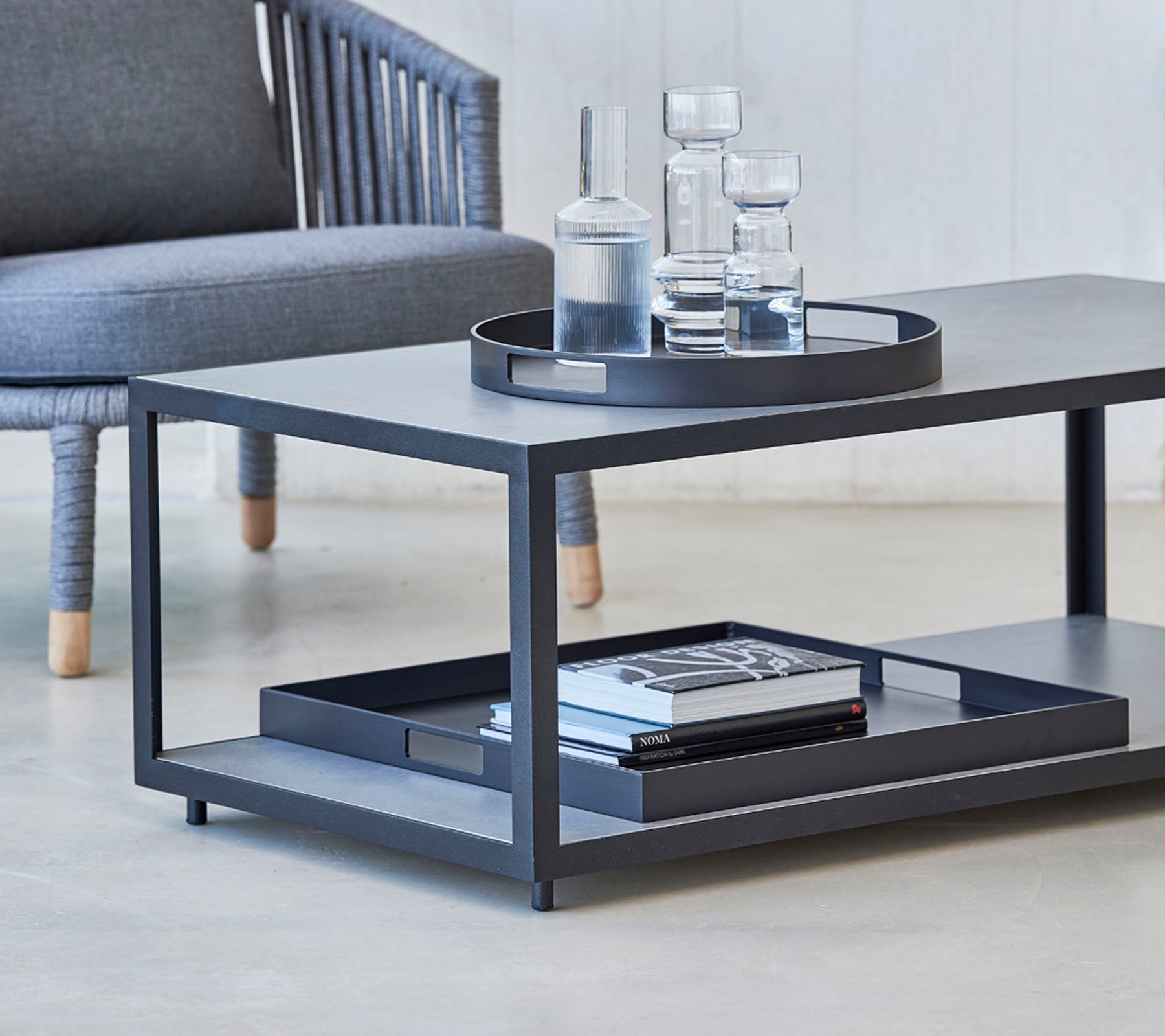 Table basse moderne au design épuré, avec un plateau, des verres et des livres sur l'étagère inférieure. Idéal pour des espaces de vie élégants.
