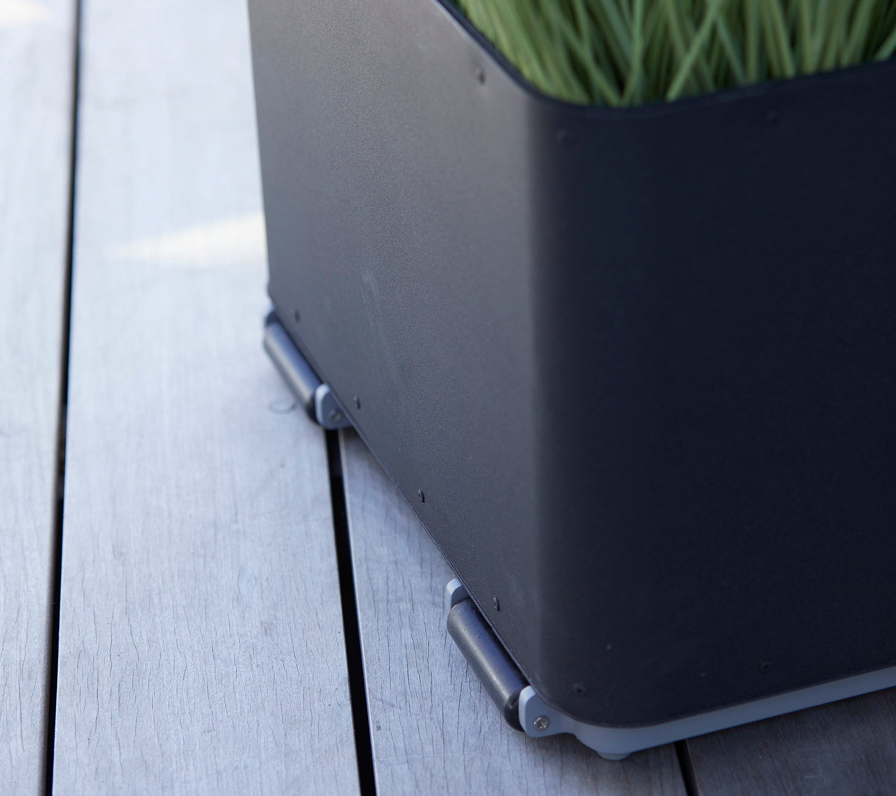 Black planter box with a sleek design, featuring green grass and silver connectors sitting on a wooden surface.