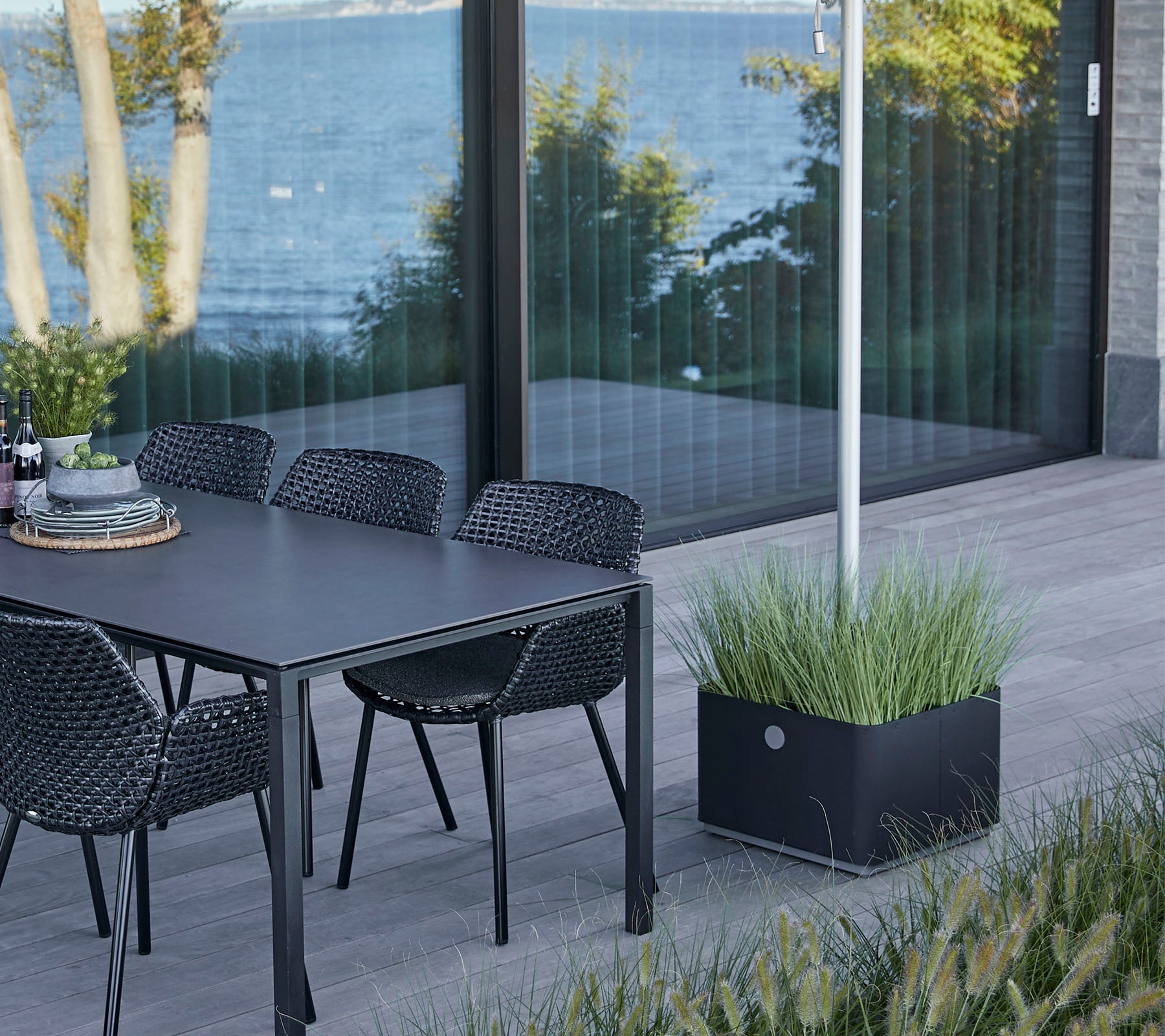 Une table élégante avec des chaises placées à côté d'une vue sur l'eau, mettant en vedette un pot décoratif avec de l'herbe luxuriante.