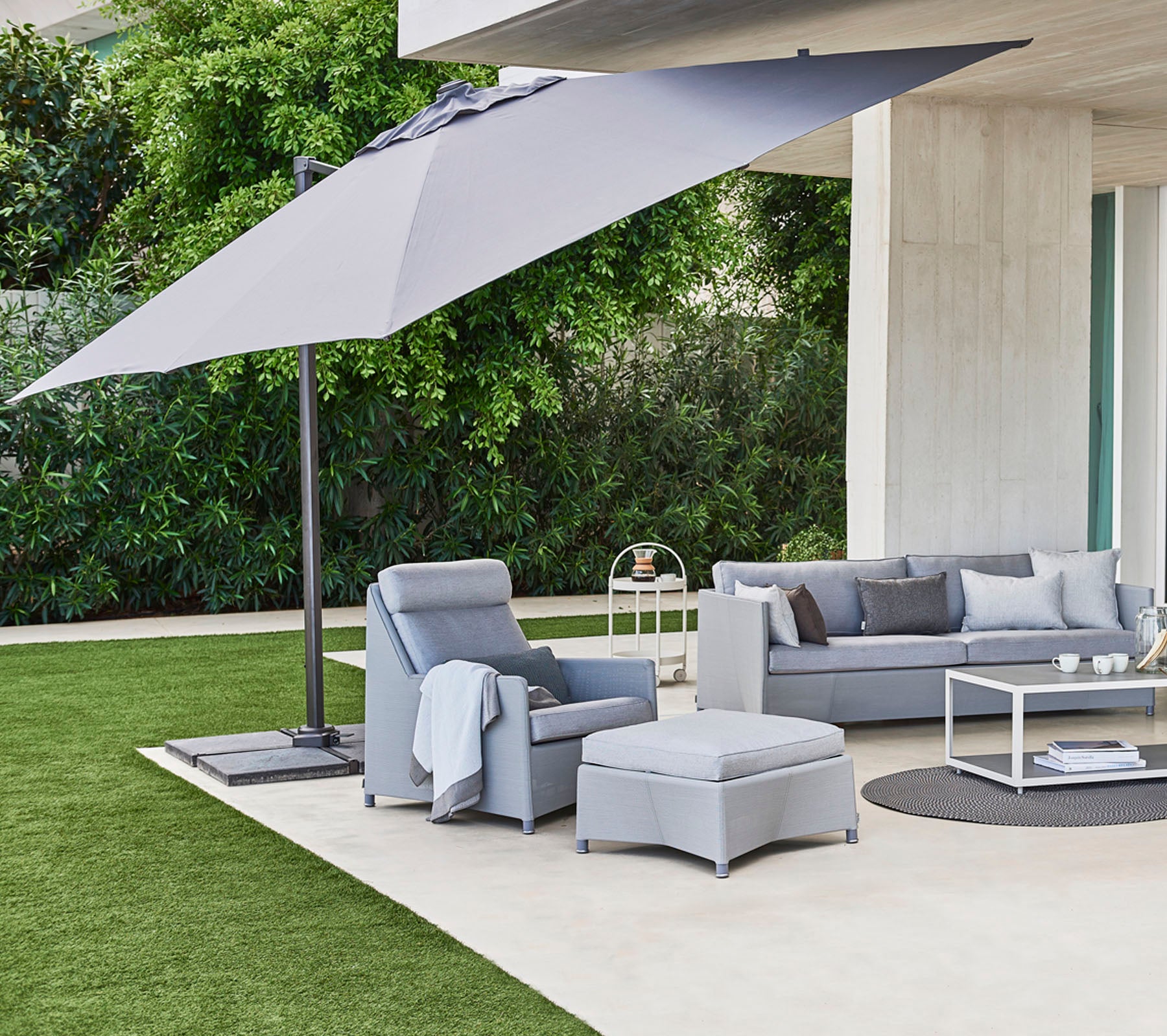 Espace extérieur chic avec des coussins moelleux, une table basse et un grand parasol offrant de l'ombre contre un fond vert.