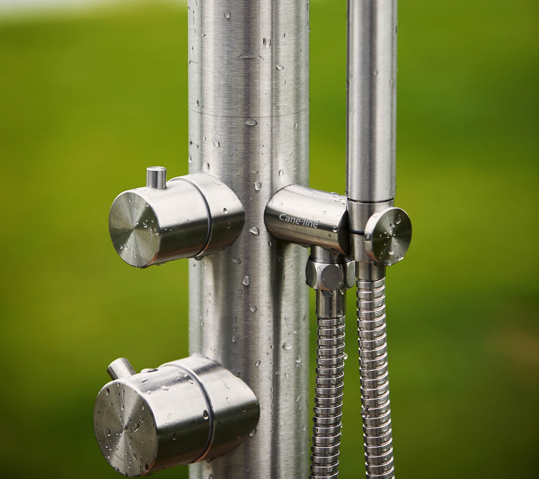 Unité de douche en acier inoxydable avec deux boutons pour le contrôle de la température et une douche à main, sur un fond vert.