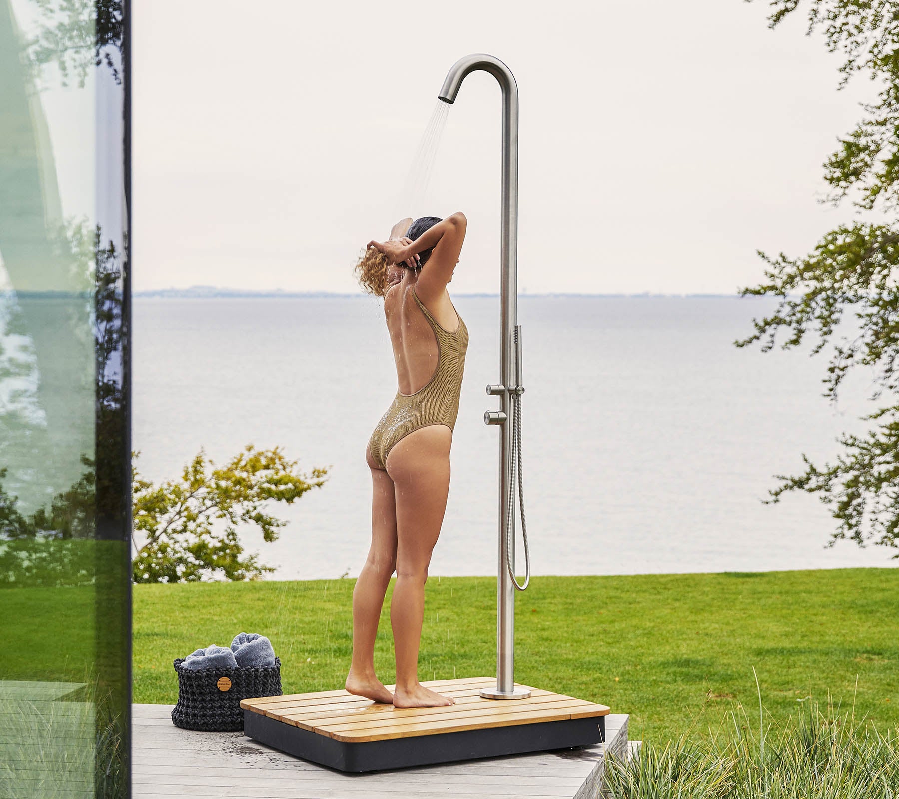 Une personne profite d'une douche extérieure rafraîchissante, debout sur une base en bois avec de l'eau ruisselant d'une douche haute et élégante.