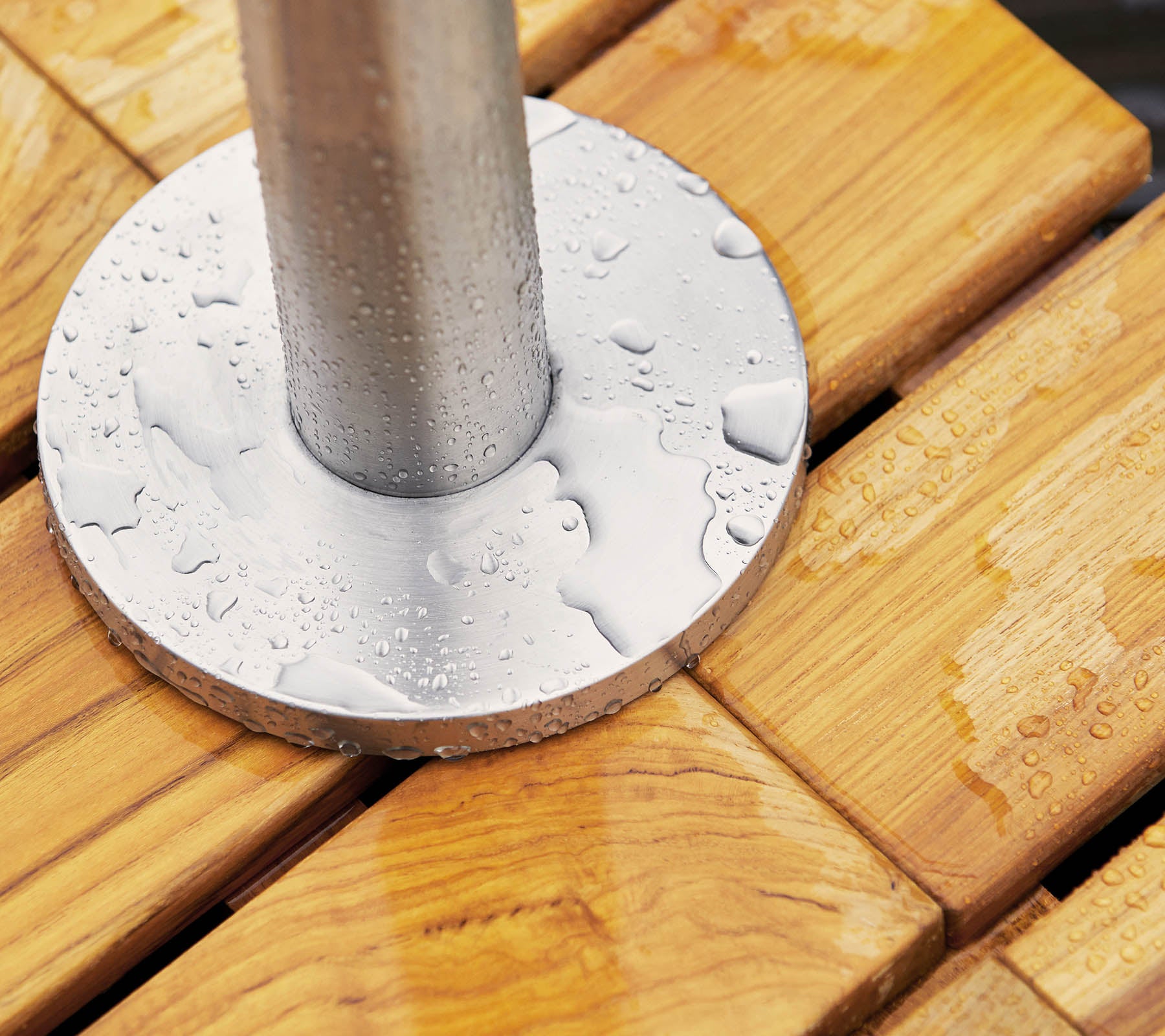 Base en métal avec des gouttes d'eau reposant sur une surface en bois, avec des planches lisses et rainurées et un poteau cylindrique au centre.