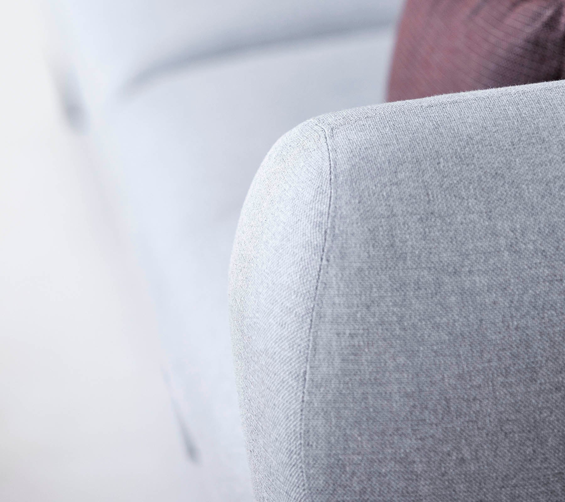 Gros plan d'un bras de sofa gris clair, présentant un tissu texturé et un design doux et arrondi, avec un soupçon d'un coussin plus sombre en arrière-plan.