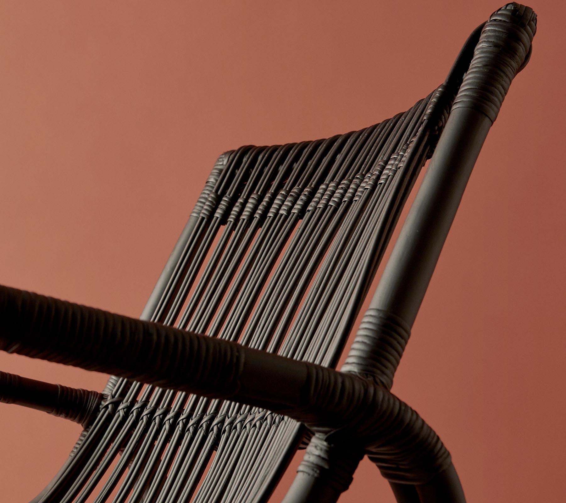 Un gros plan d'un dossier de chaise tissé sur un fond de couleur chaude, mettant en valeur son design et sa texture complexes.