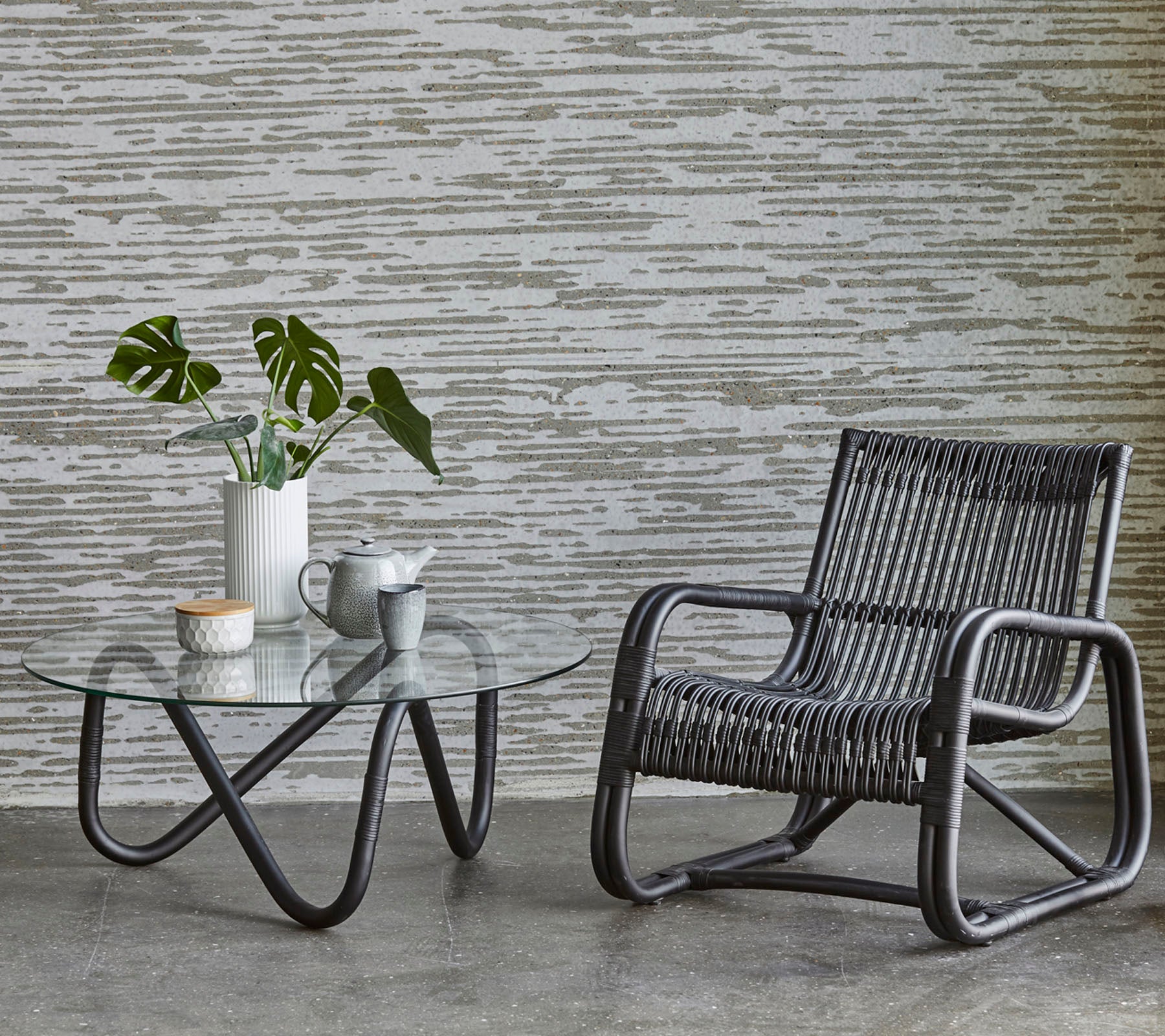 Une chaise élégante et une table en verre avec une plante et un service à café, complétée par un mur texturé en arrière-plan.