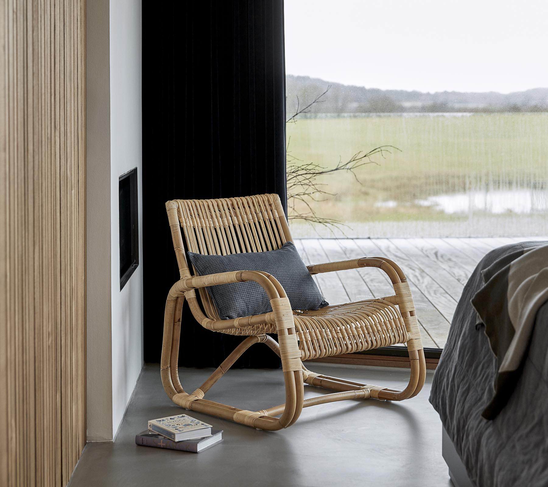 Un rocking chair élégant en matériaux naturels, placé à côté d'un lit et d'un livre, avec une vue pittoresque visible à travers de grandes fenêtres.