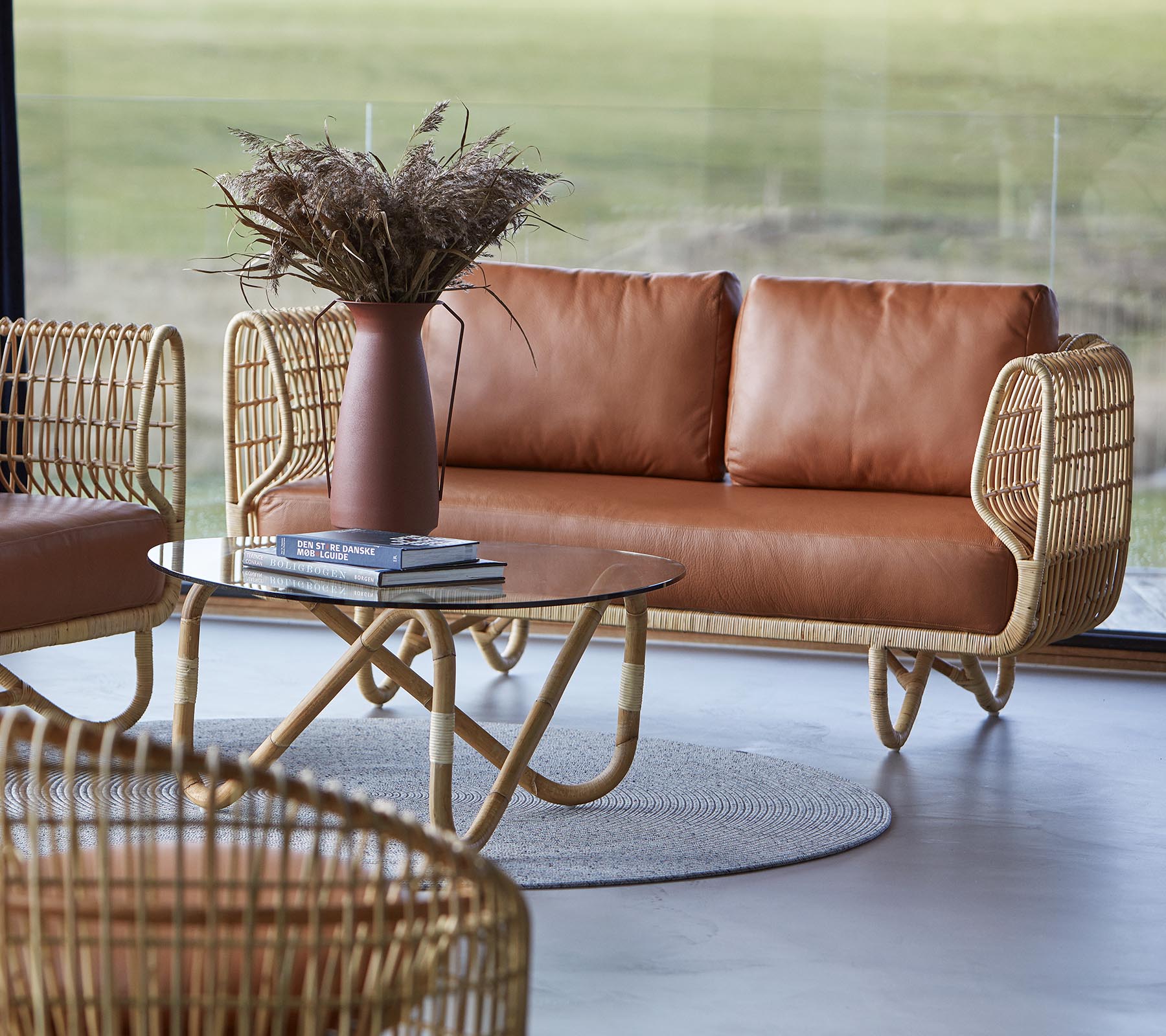 Un coin salon élégant avec un canapé en cuir brun, une table basse ronde et des éléments décoratifs comme un vase avec des fleurs séchées.