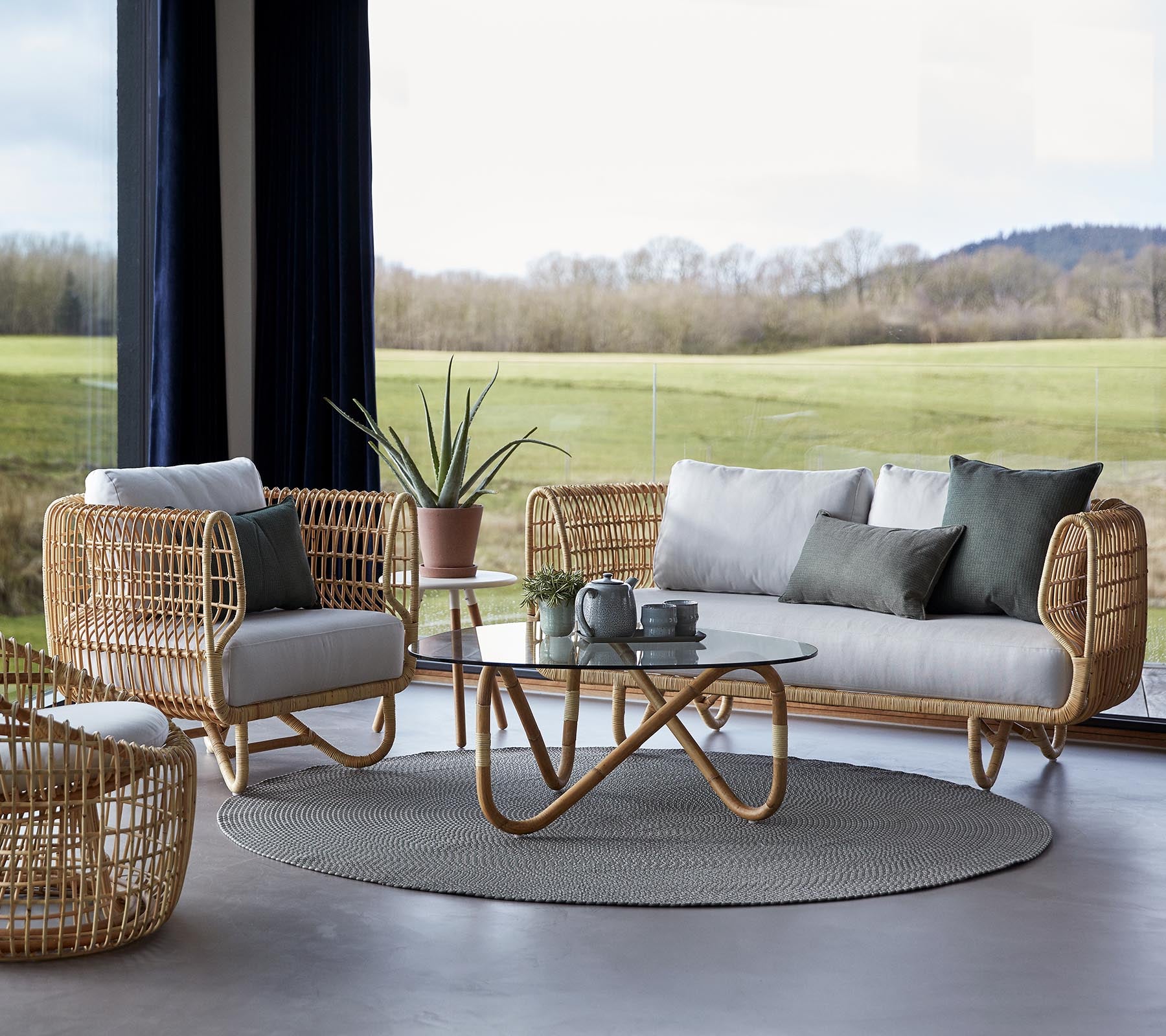 Un agencement de sièges élégant avec des meubles tressés, un tapis rond et une table basse en verre, complété par des éléments de décoration minimalistes.