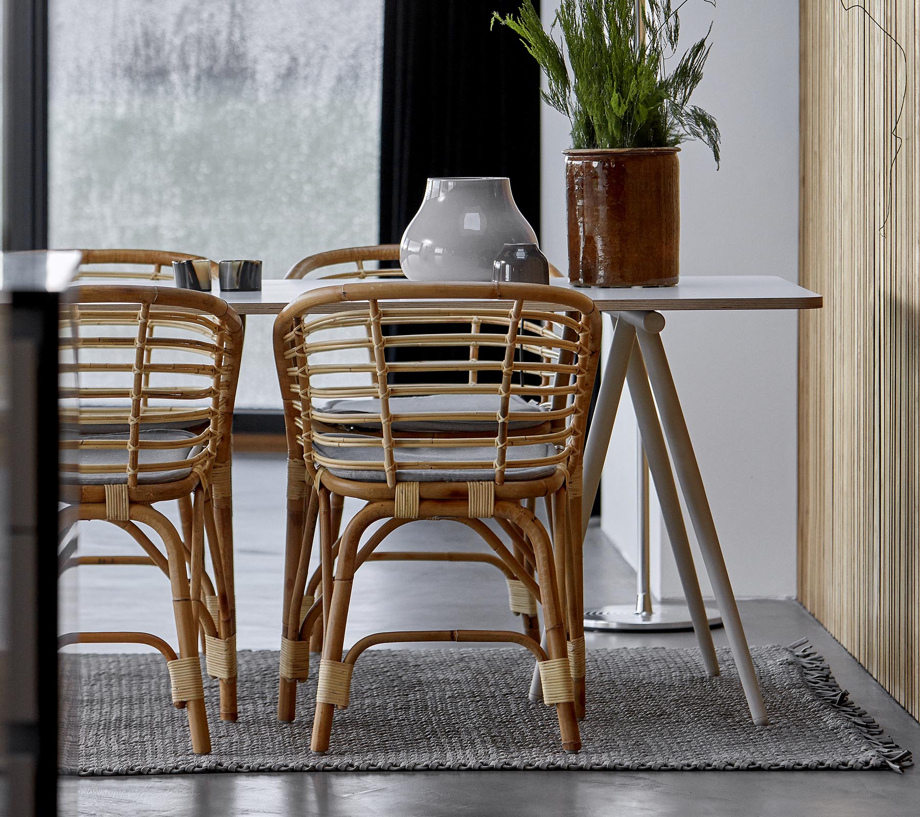 Un aménagement de salle à manger moderne avec des chaises en rotin, une table élégante et des plantes décoratives dans un intérieur stylé.