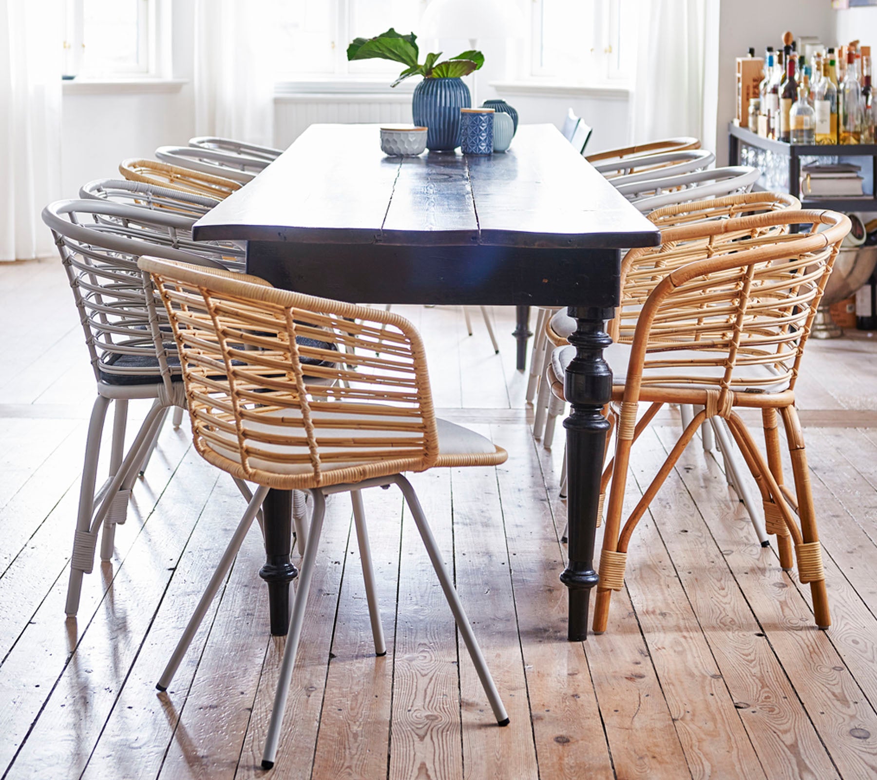 Une table en bois entourée de chaises tissées élégantes dans des tons clairs et foncés, avec une petite plante et une tasse sur le dessus.