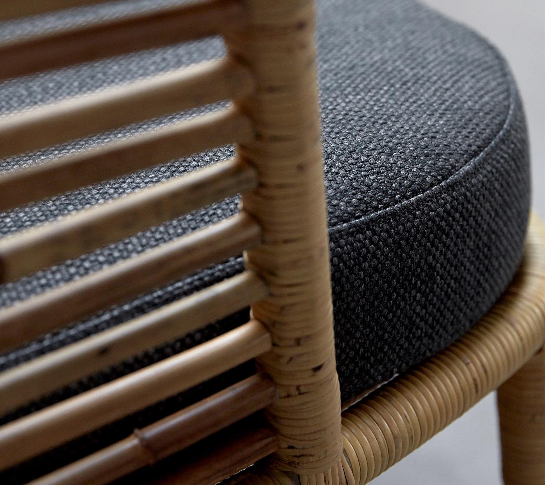 Gros plan d'une chaise tissée avec un coussin rond gris foncé et un cadre en bois naturel mettant en valeur des détails complexes.