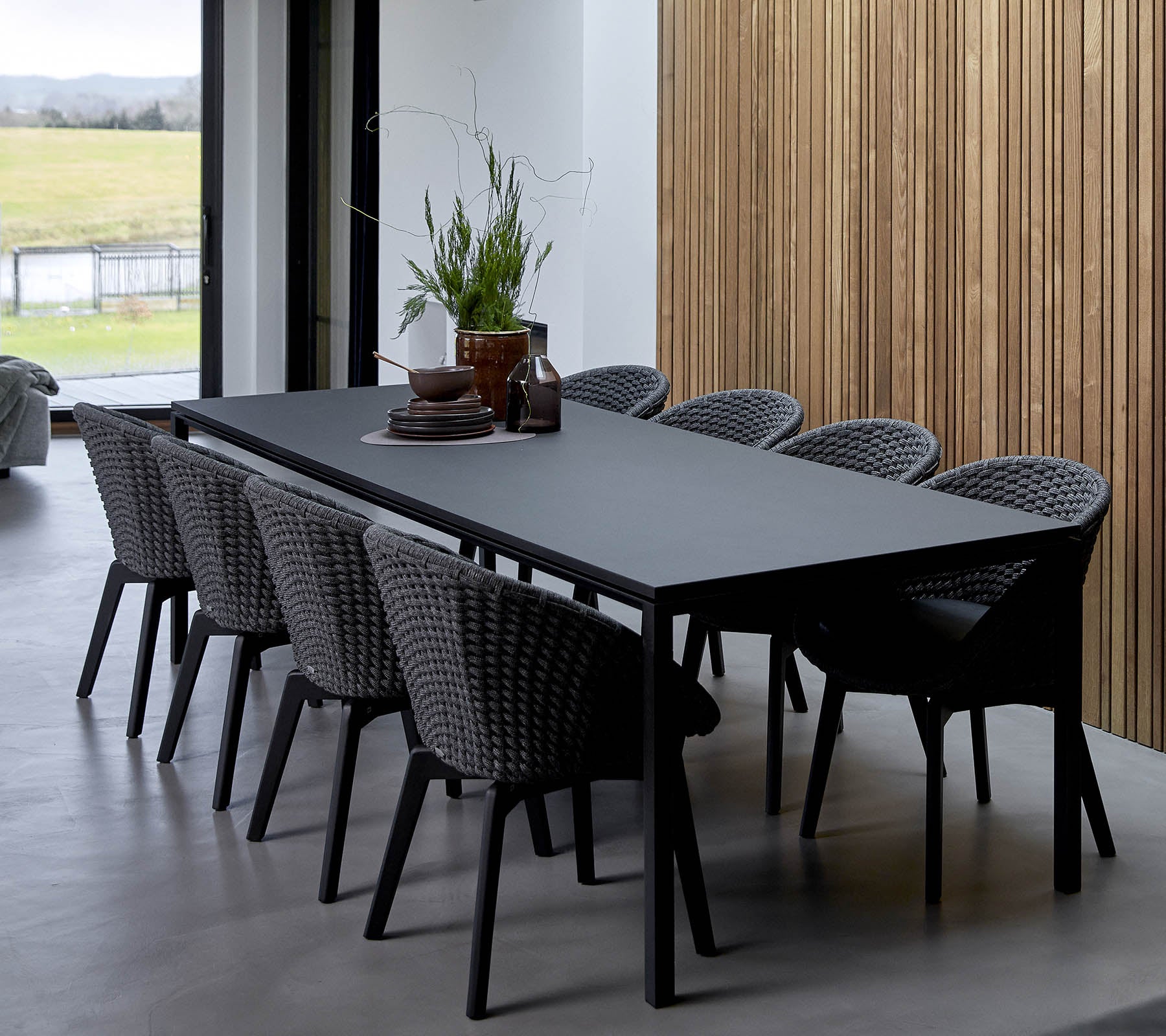 Une table élégante entourée de chaises tressées, ornée de plantes décoratives et d'un centre de table, contre un fond en bois.