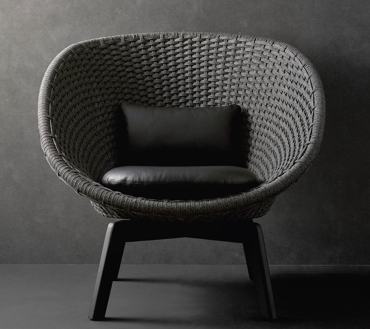 Une chaise ronde élégante avec un design tissé texturé et un coussin noir, reposant sur des pieds en bois élégants contre un fond sombre.