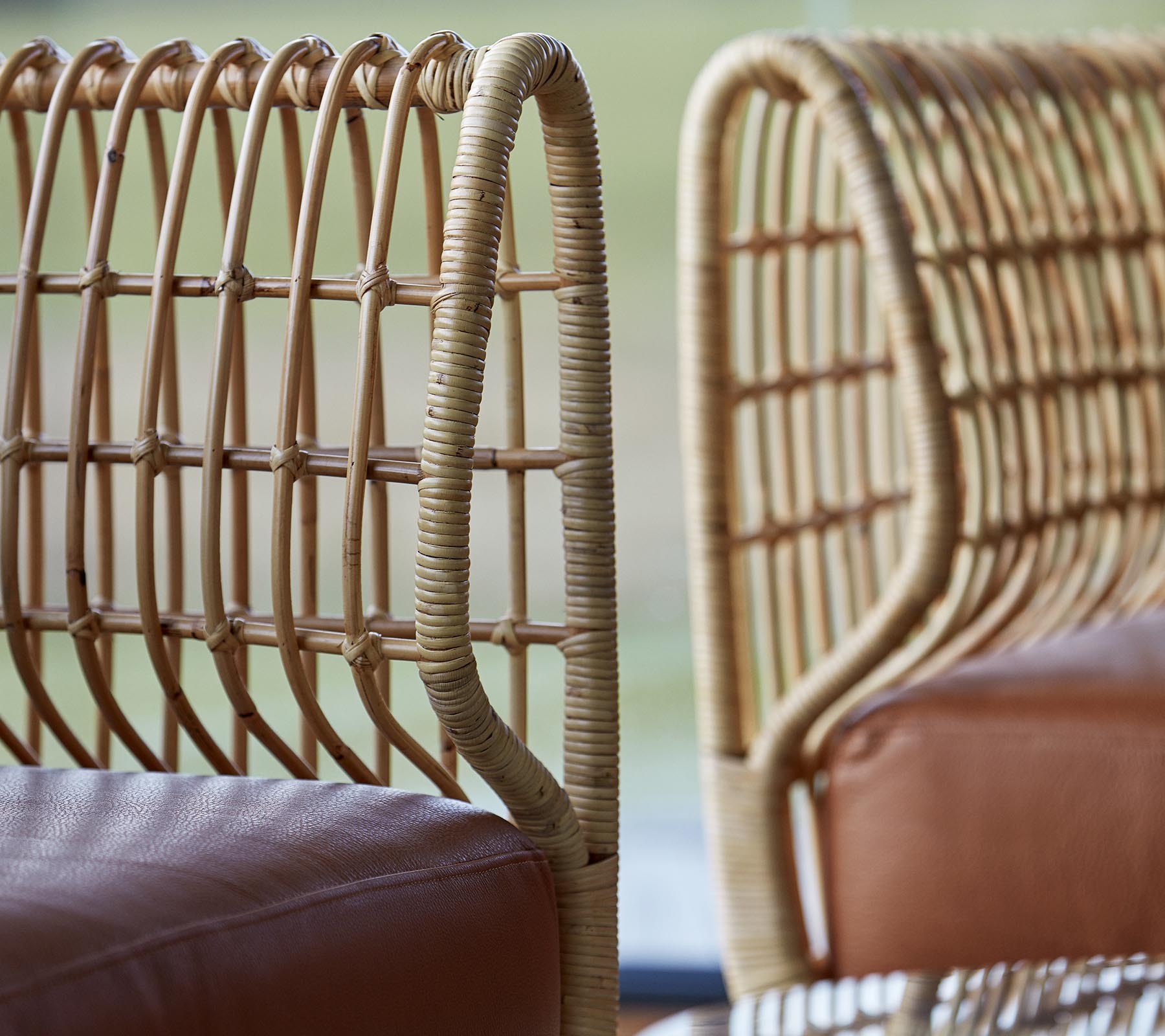 Deux chaises élégantes avec des dossiers en rotin tressé et des sièges en cuir lisse, mettant en valeur une esthétique de design moderne.