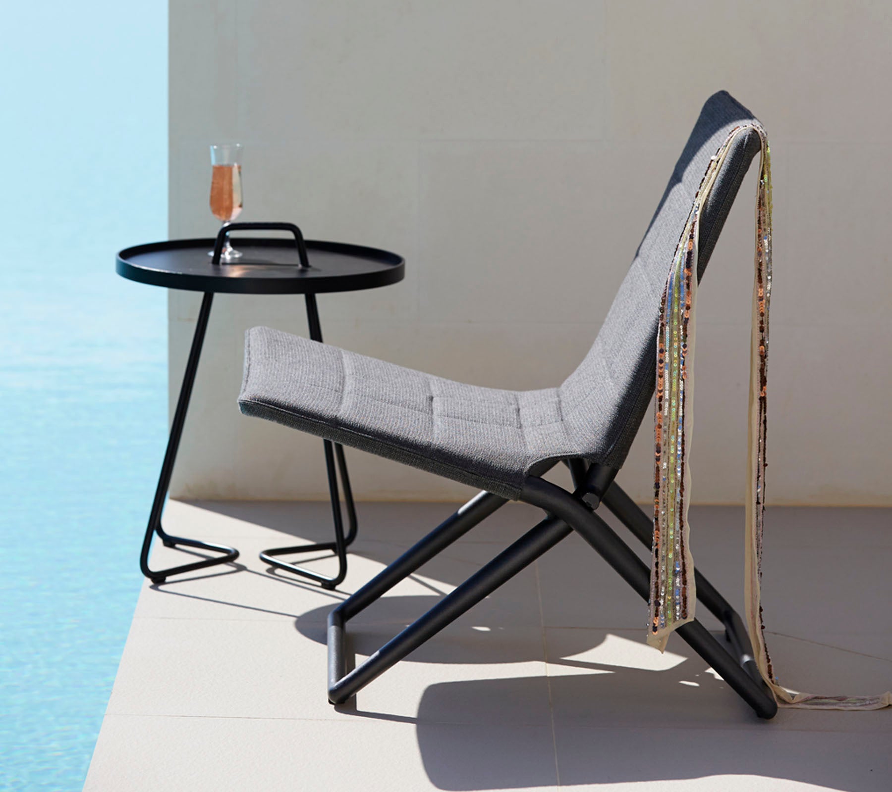 Une chaise élégante avec un tissu gris et un cadre en métal noir épuré, assortie d'une table ronde tenant une boisson et des perles décoratives.