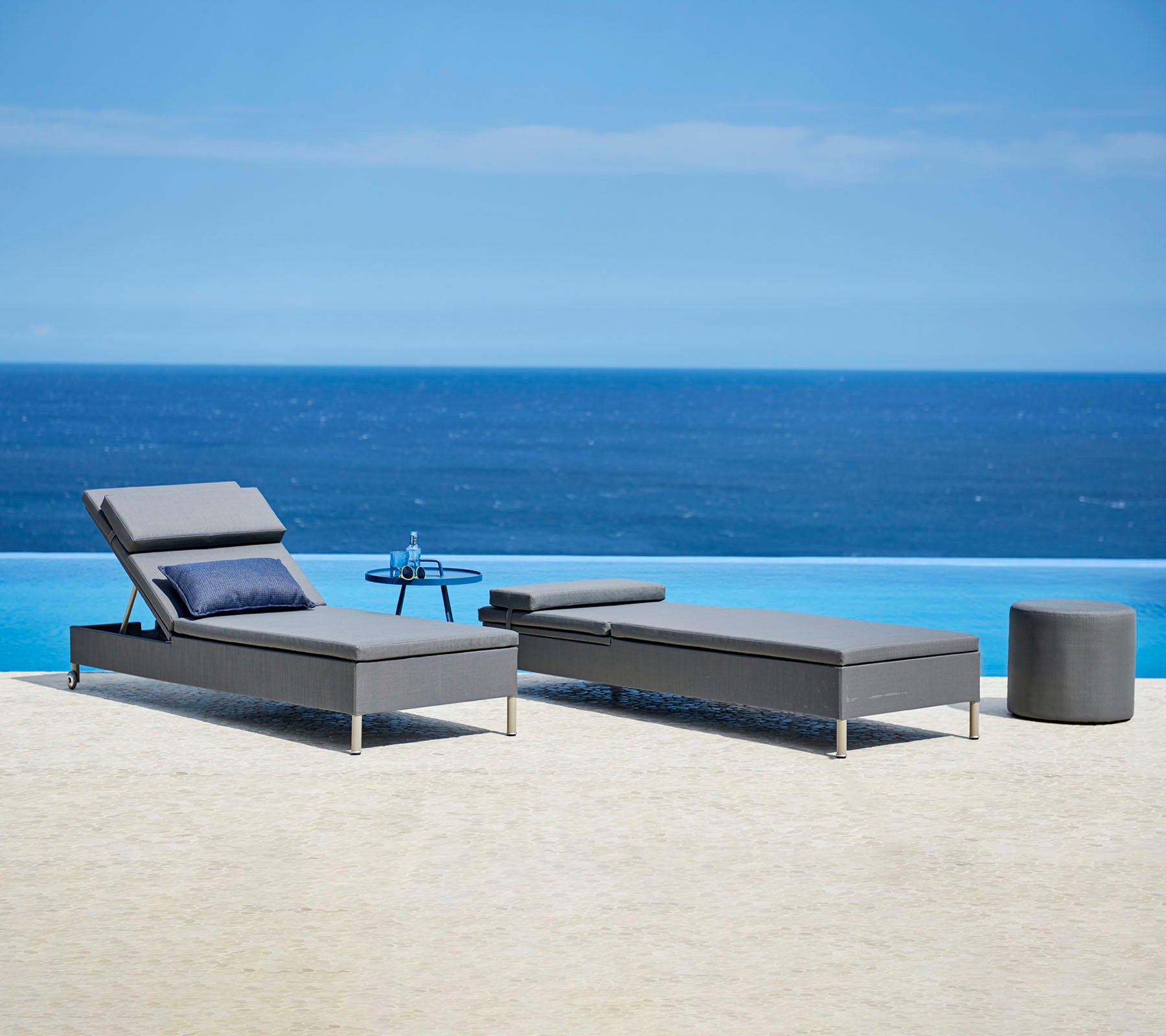 Deux fauteuils gris élégants avec des coussins et une petite table d'appoint près d'une paisible fontaine bleue, parfaits pour la détente.