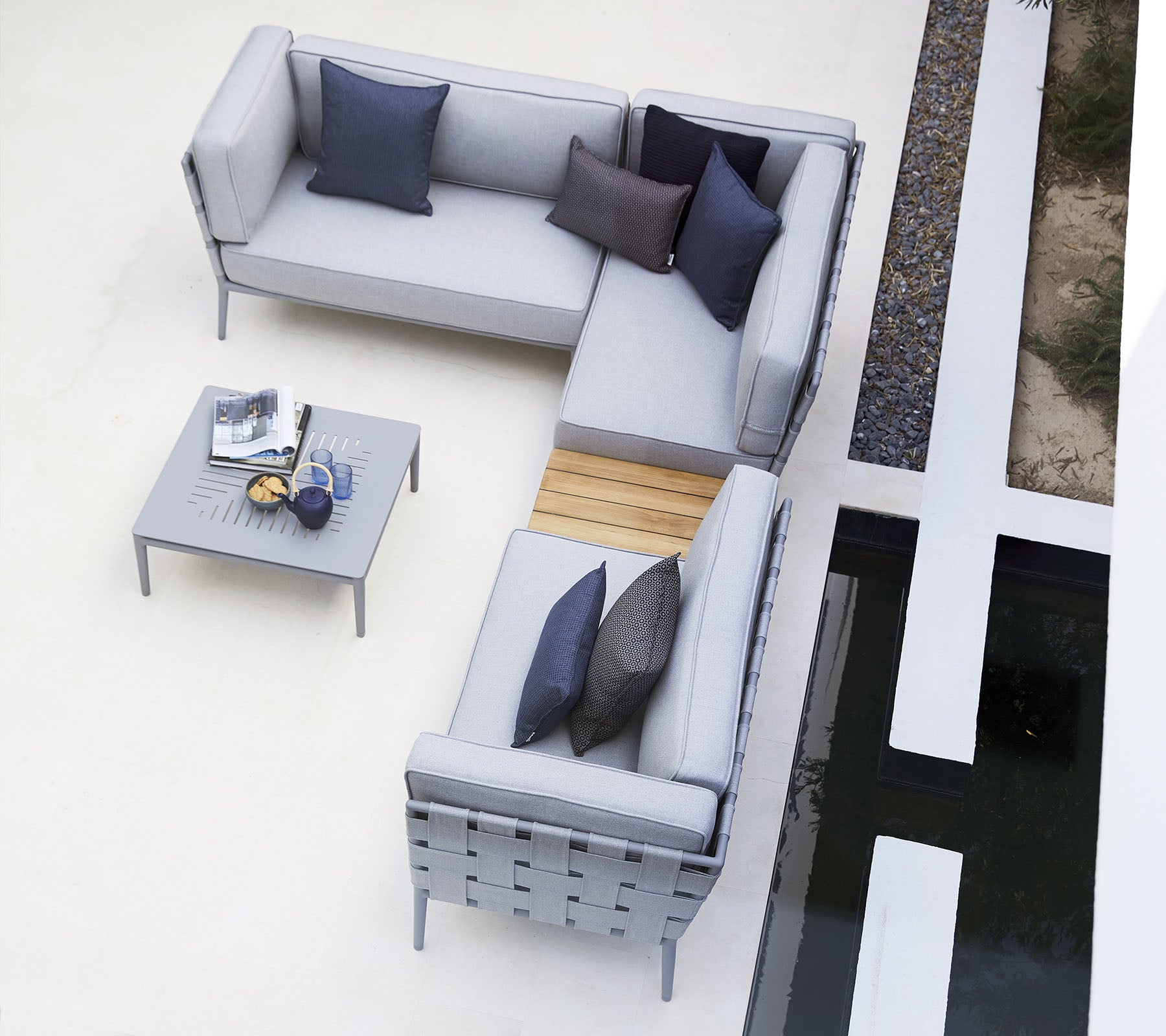 Agencement de sièges d'extérieur moderne avec des coussins gris, rehaussé par des coussins sombres, complété par une table minimaliste.
