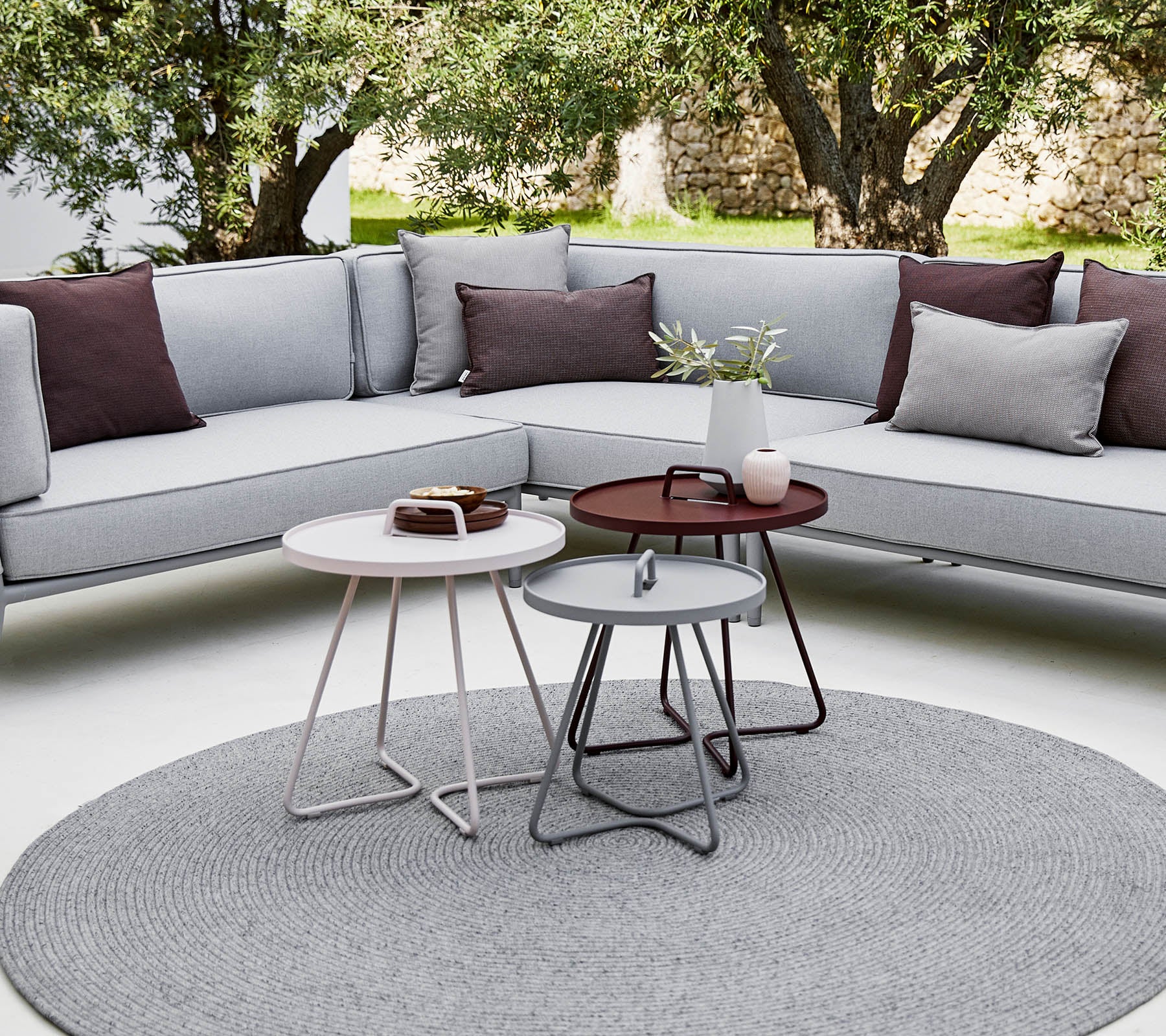 Espace extérieur élégant avec un canapé sectionnel avec des coussins et des tables basses rondes modernes dans un cadre relaxant et contemporain.