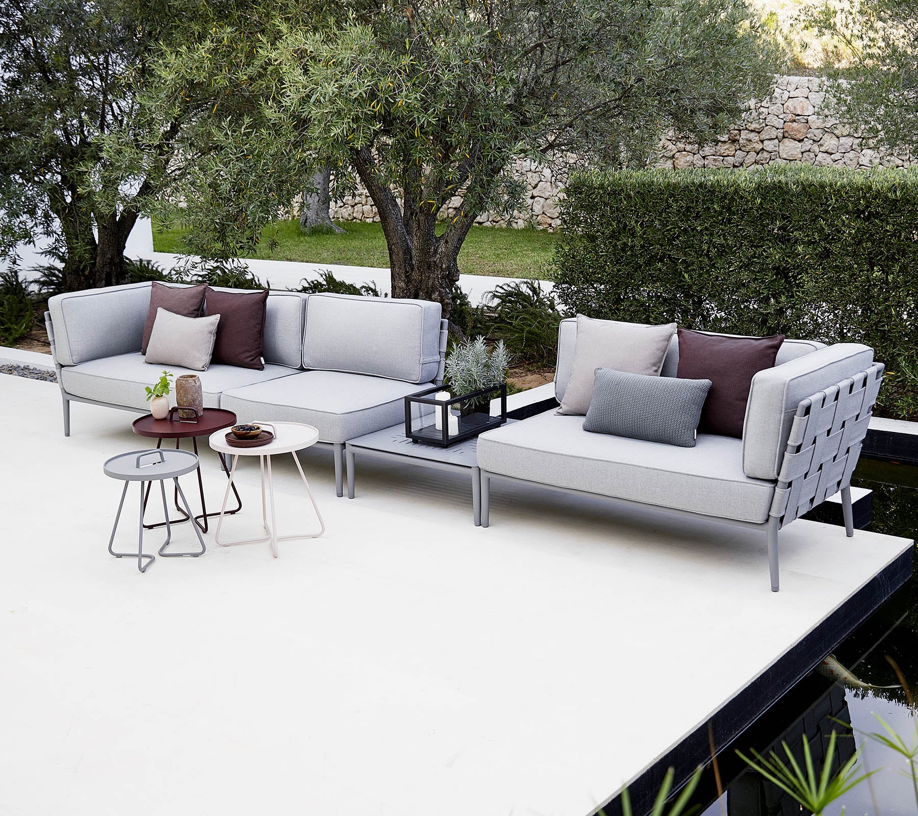 Aménagement moderne de sièges extérieurs avec des coussins, accompagné d'une table d'appoint élégante et de plantes décoratives.