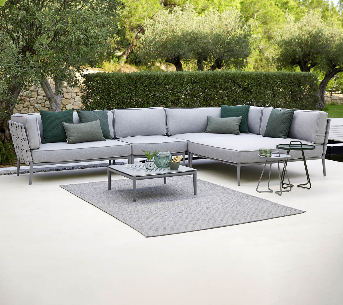 Canapé d'extérieur élégant avec des coussins verts, une table basse et un tapis, sur fond de verdure.