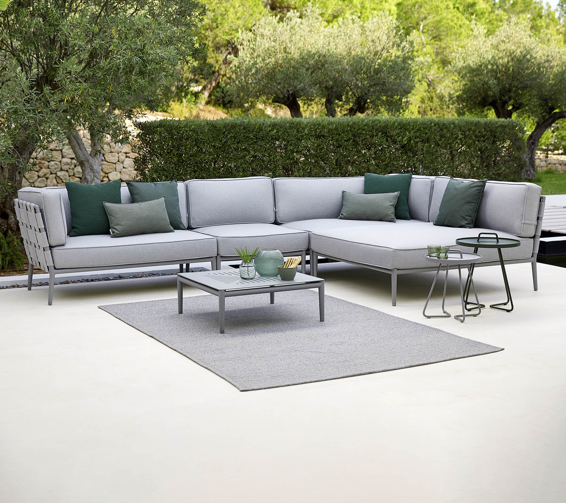 Canapé d'extérieur élégant avec des coussins verts, une table basse et un tapis, sur fond de verdure.