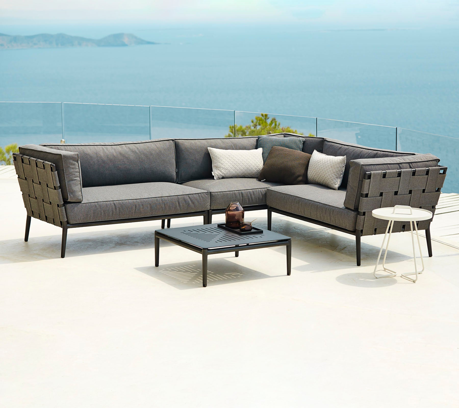 Aménagement moderne de sièges extérieurs comprenant un canapé sectionnel avec des coussins et une table basse, sur fond de paysage aquatique.